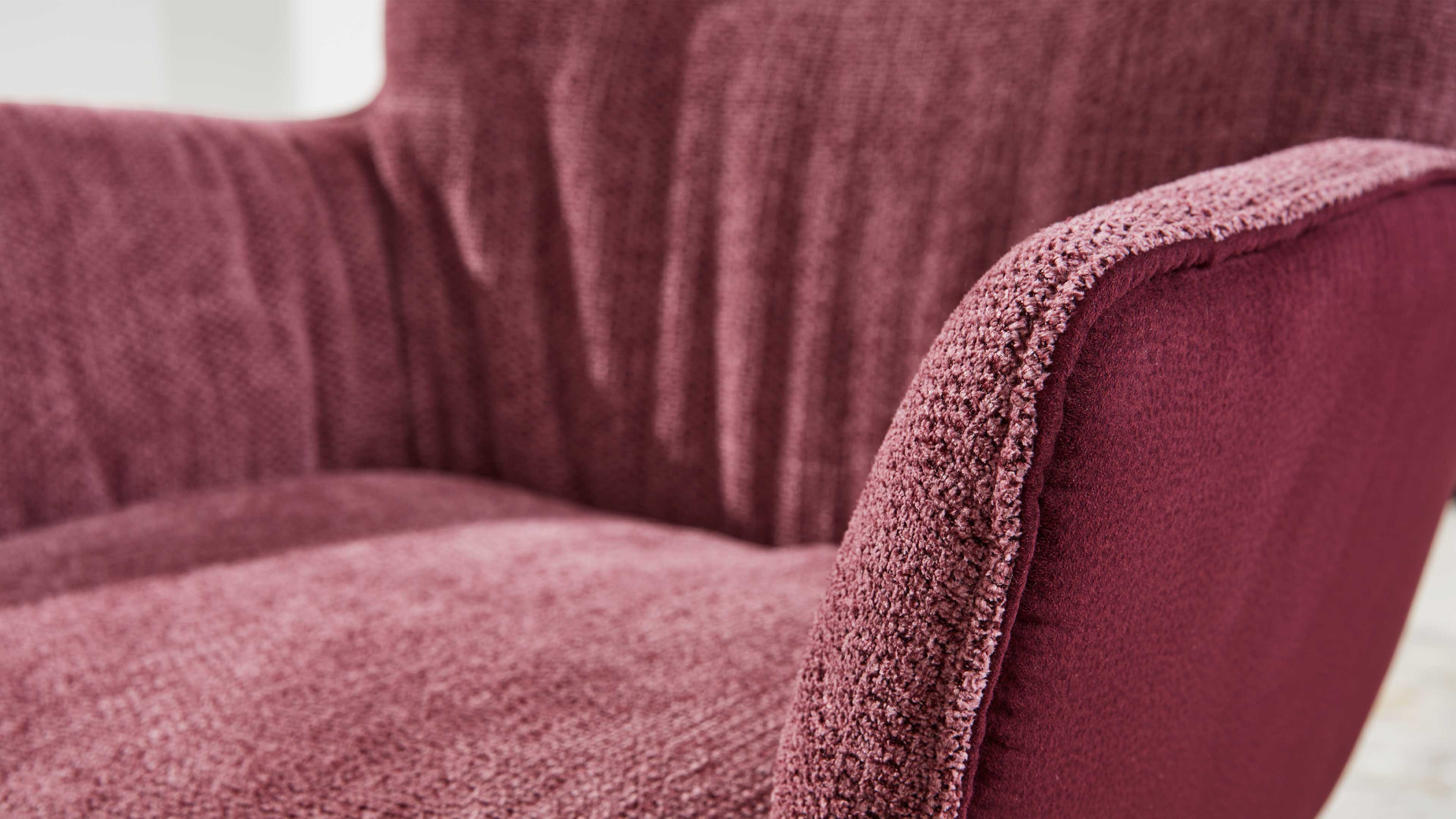 Gepolsterte Nahaufnahme eines bordeauxfarbenen Sessels mit gerundeter Armlehne, sichtbarer Naht und unterschiedlicher Stoffstruktur.