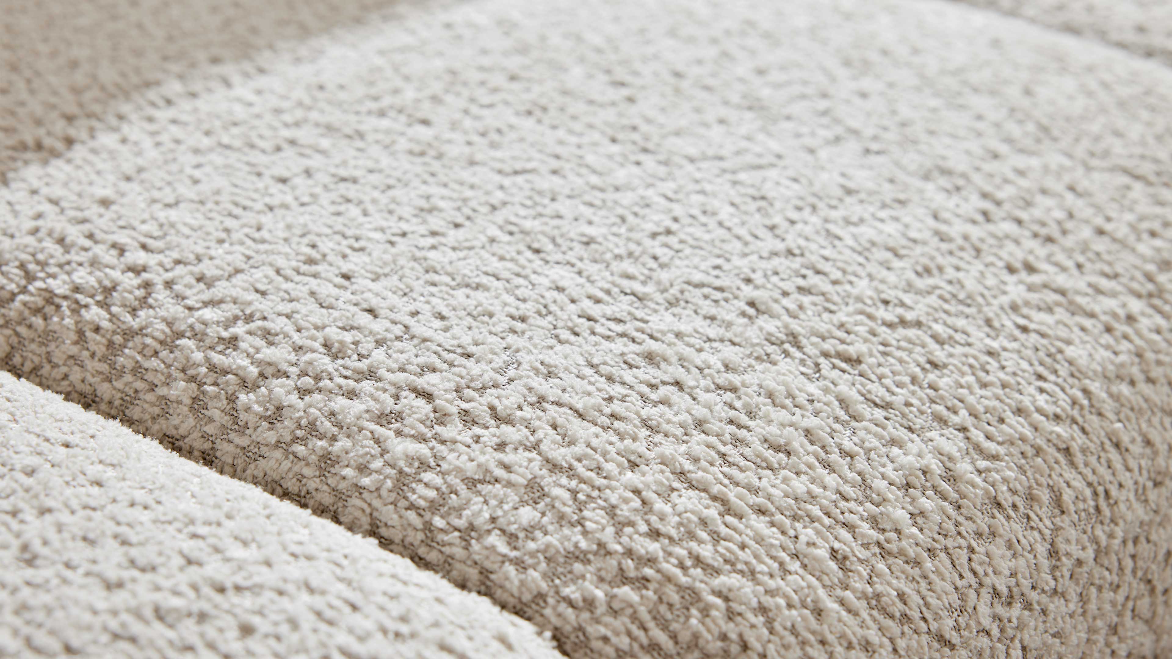 Nahaufnahme einer cremefarbenen, dicht geschlungenen Bouclé-Polsteroberfläche mit drei parallel verlaufenden Kanten.