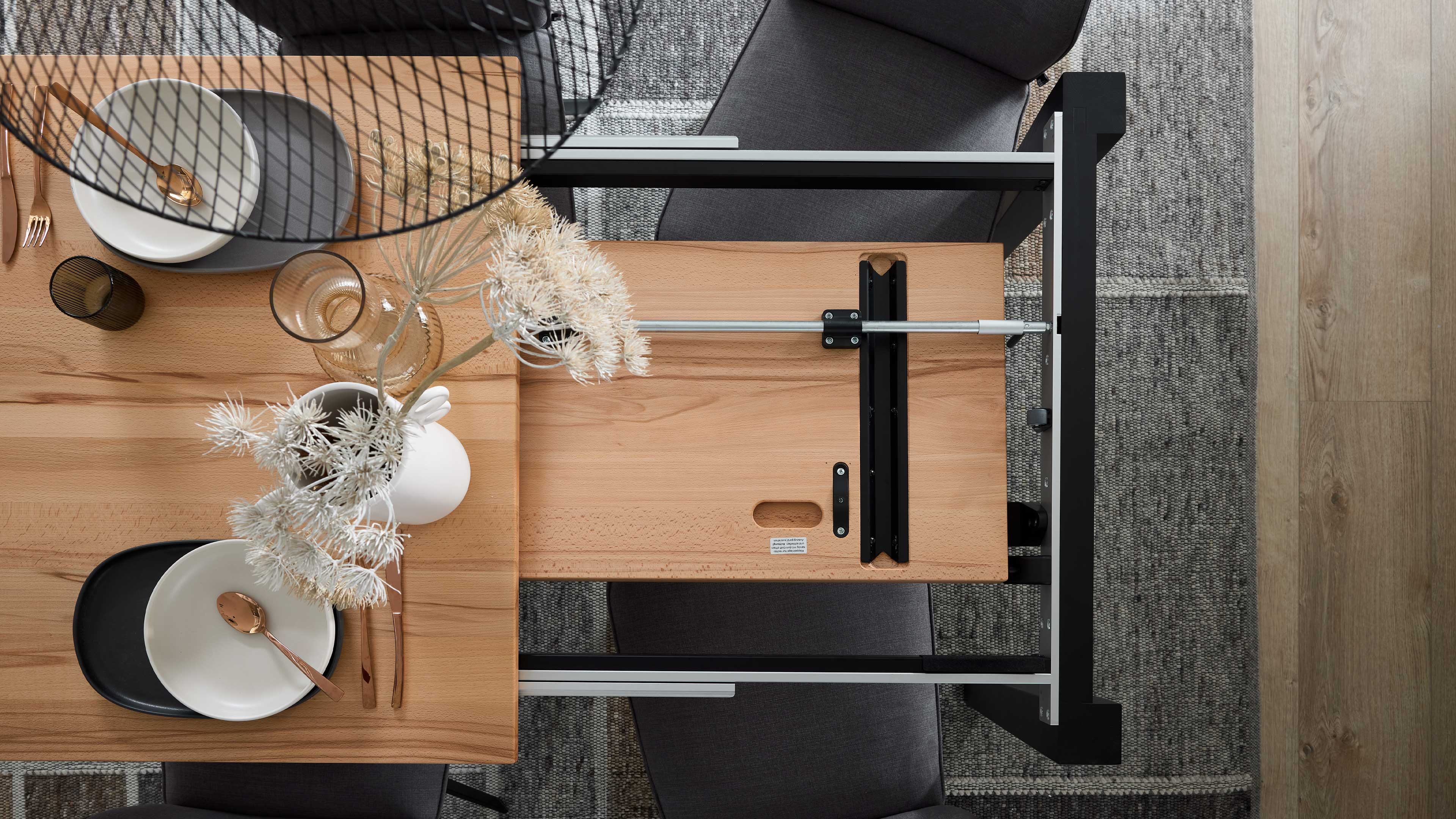 Ausgezogene helle Holz-Tischplatte mit sichtbarer schwarzer Metallverlängerungsmechanik, Tellern, Besteck, Glasvasen und getrockneten Blumen.