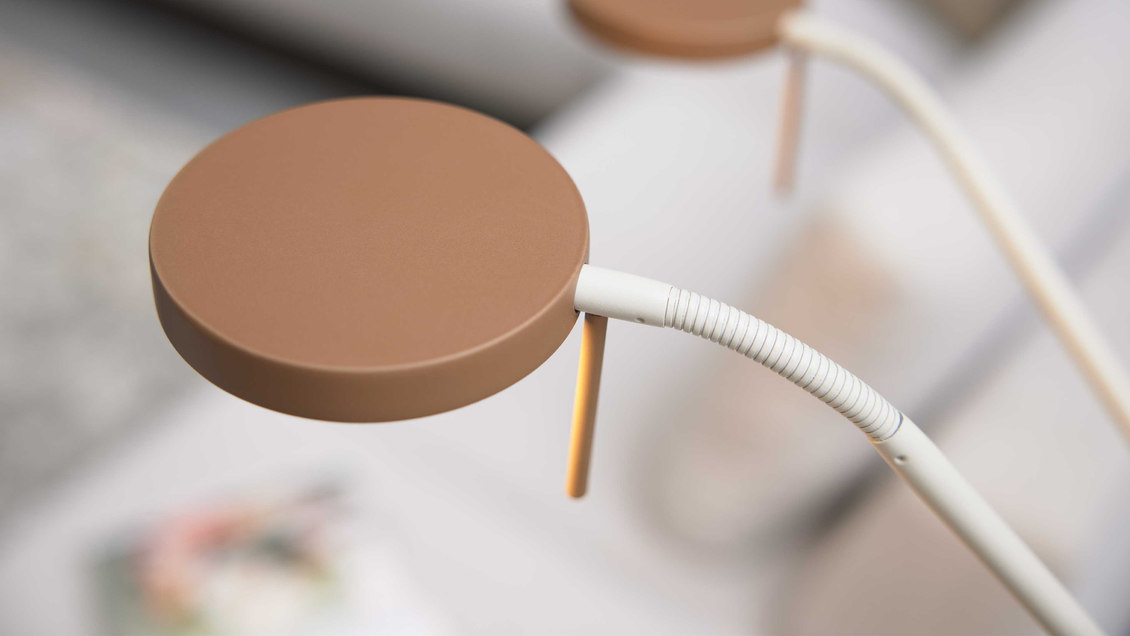 Runde braune Lampenplatte mit weißem, geripptem Schwanenhals, dünnem orangfarbenem Stab und unscharfem Hintergrund.