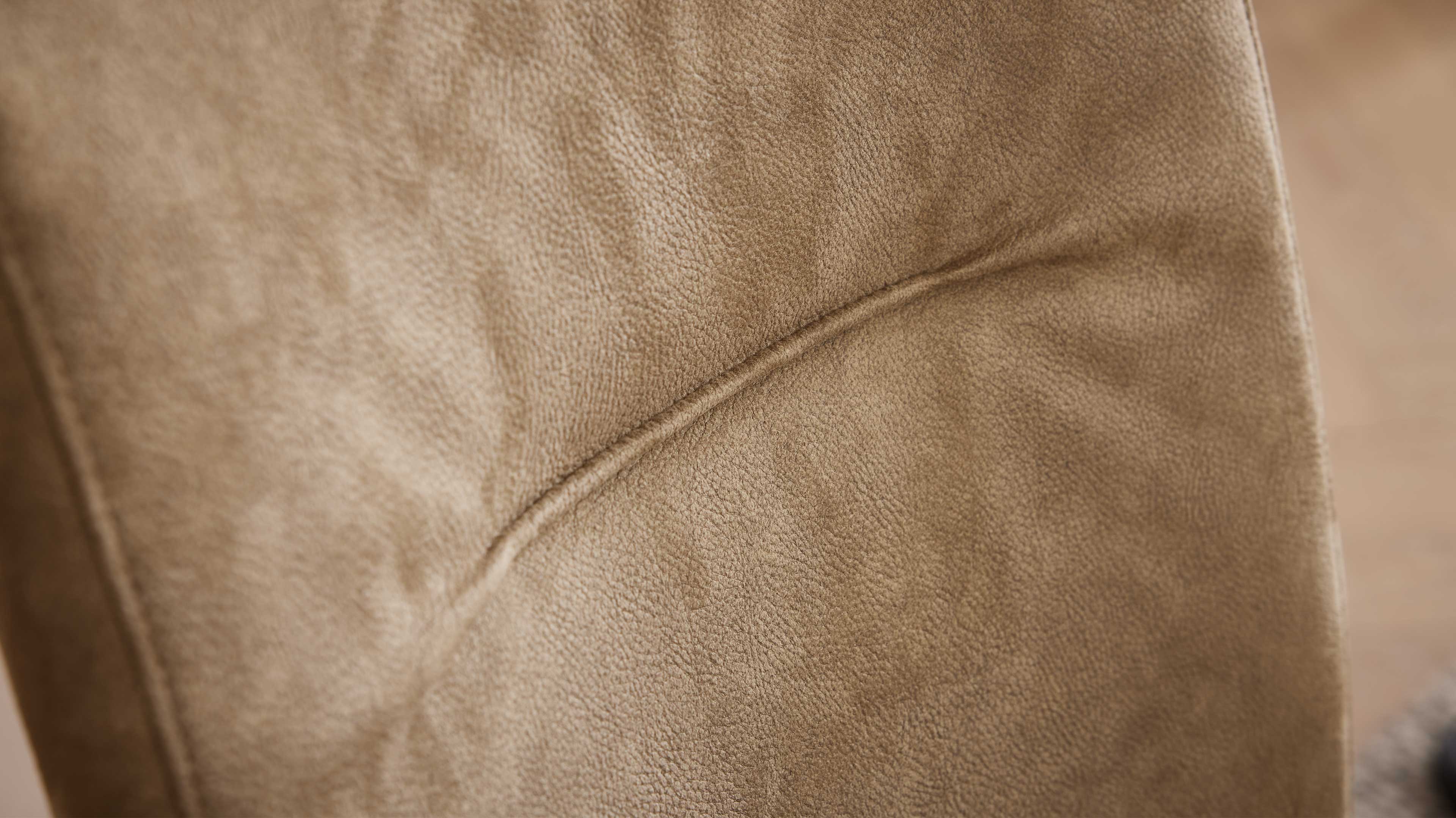 Nahaufnahme einer hellbraunen Polsterfläche mit feiner Narbung, sichtbarer Naht und leichten Falten.