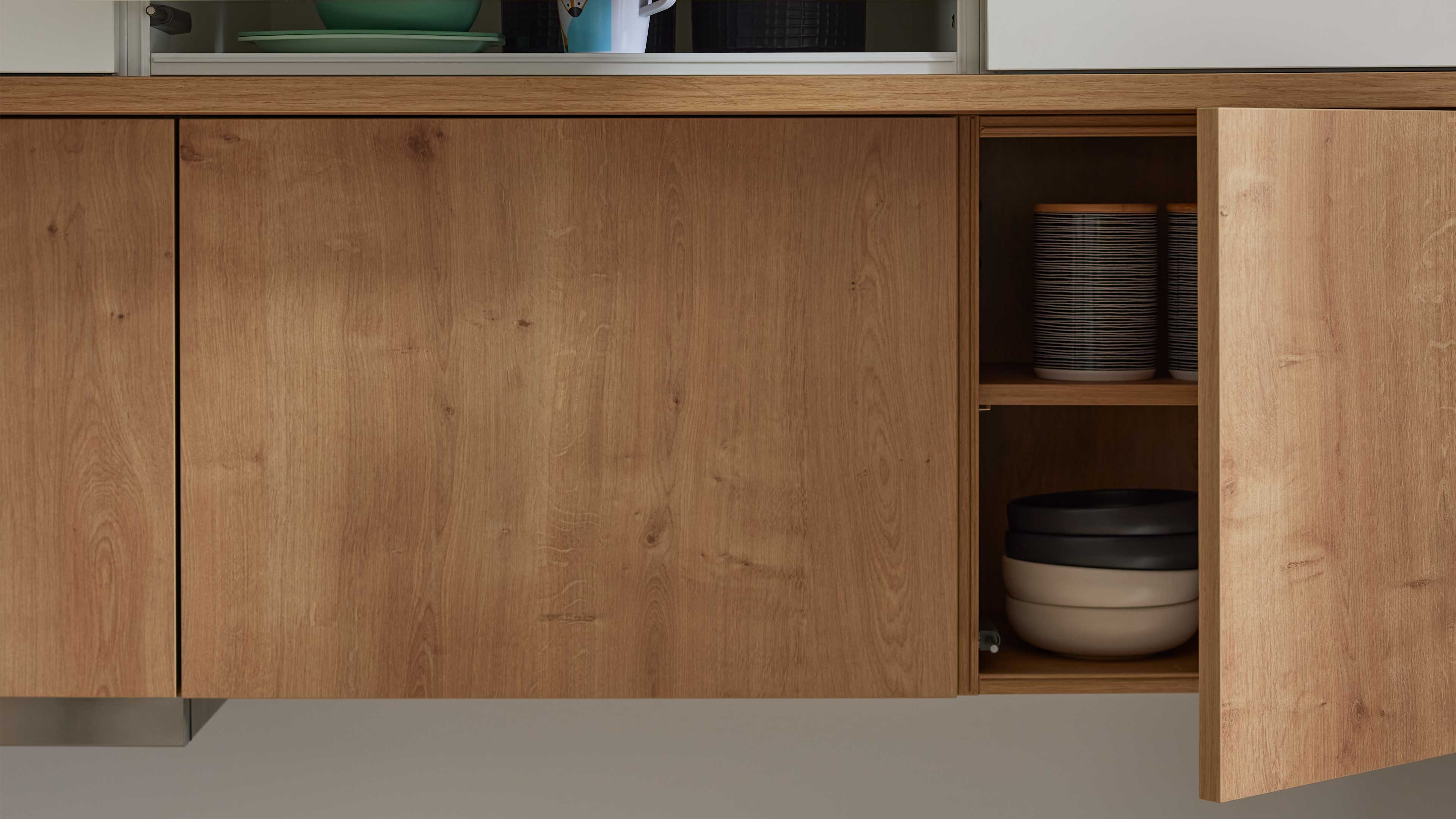 Niedriges Holz-Küchenschrankmodul mit geöffneter rechter Tür und innen sichtbaren gestapelten Schalen und gestreiften Vorratsdosen.