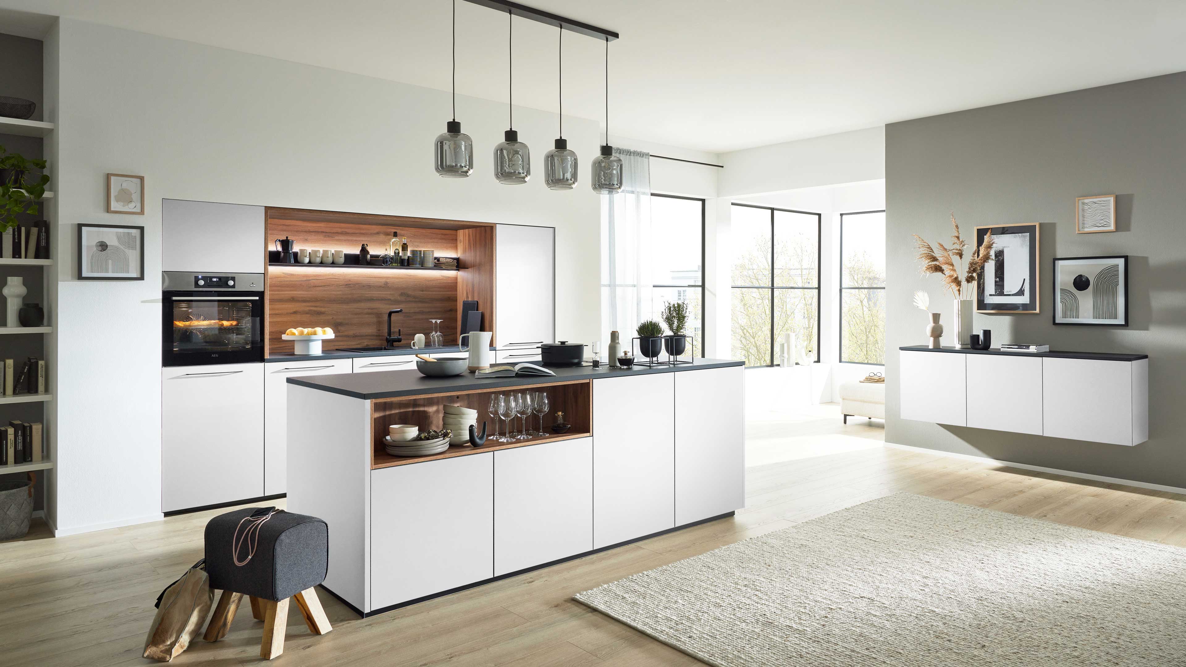 Weiße Kücheninsel mit dunkler Arbeitsplatte und offenem Holzfach, dahinter Ofen, fünf Glas-Hängelampen und ein schwebendes Sideboard.