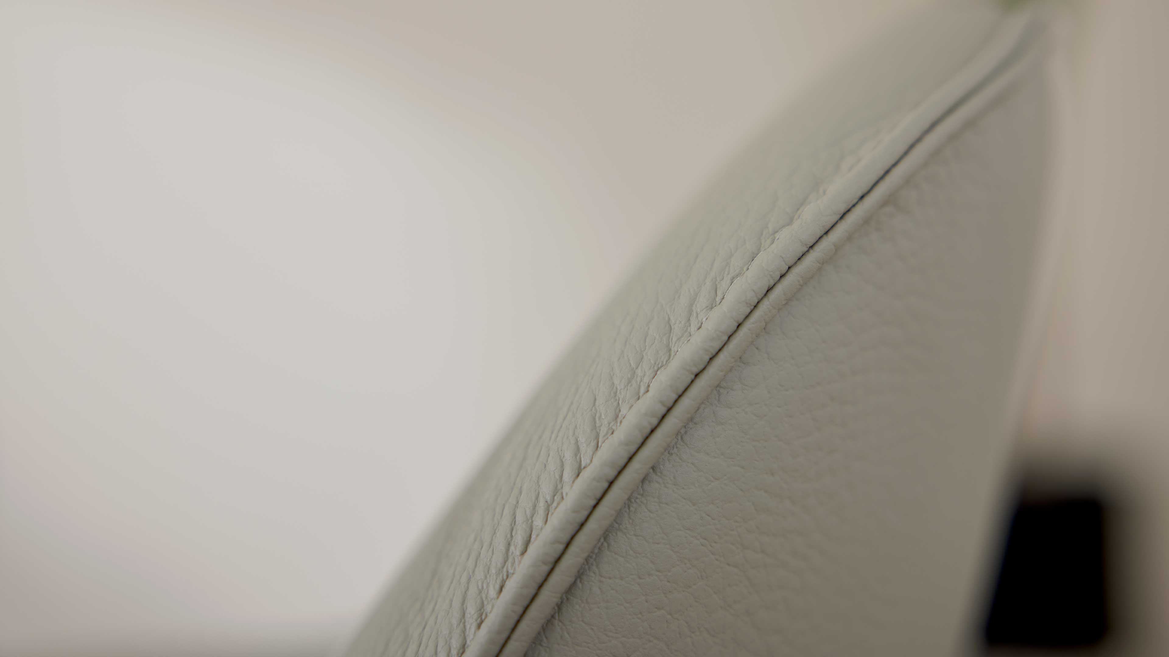 Nahaufnahme einer hellgrauen Lederpolsterung mit sichtbarer Ziernaht und feiner, körniger Struktur entlang der Kante.