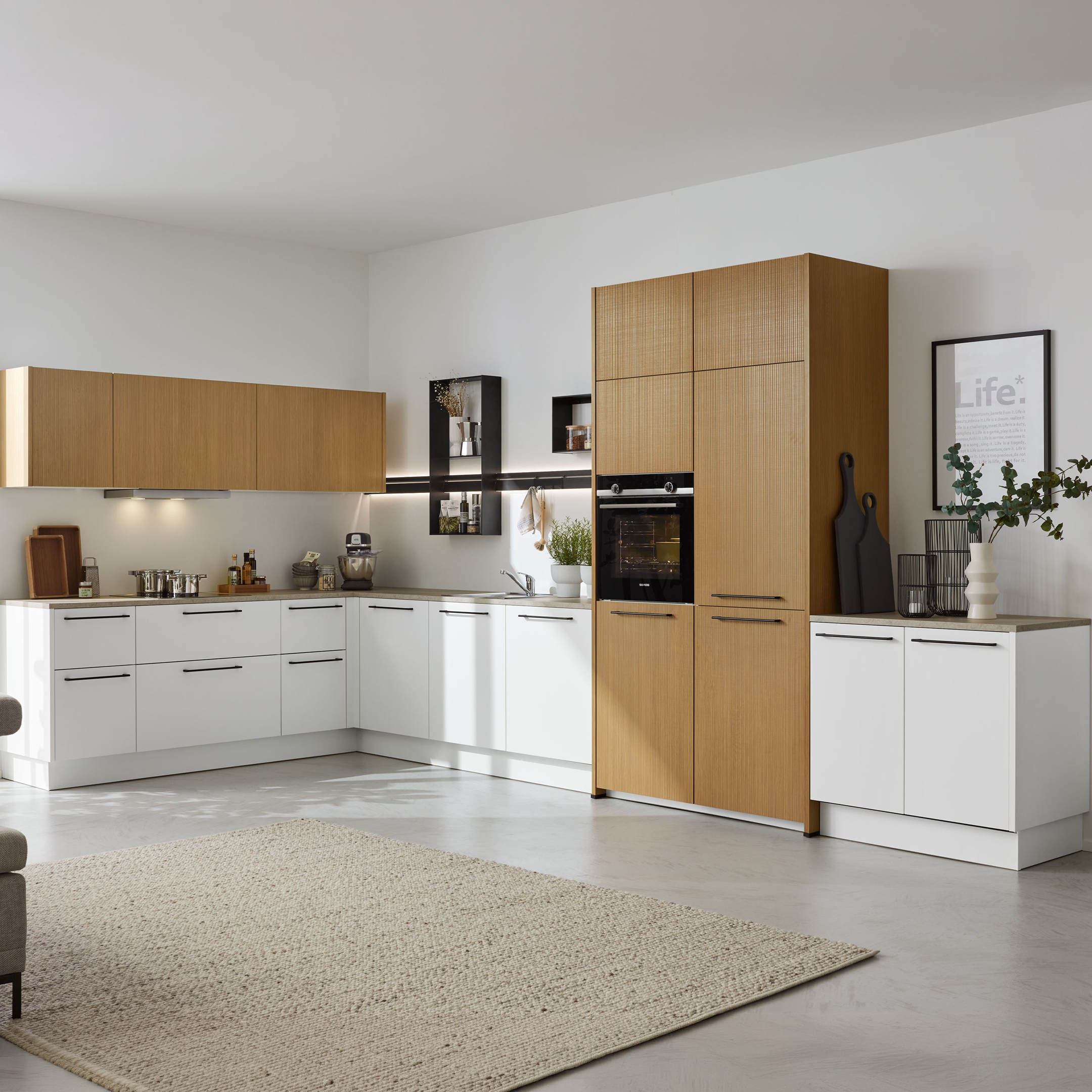 L-förmige Küche mit weißen Unterschränken und Holzfronten, Holzschrank mit eingebautem Backofen, offenen Regalen, links Sofa, große Fenster.