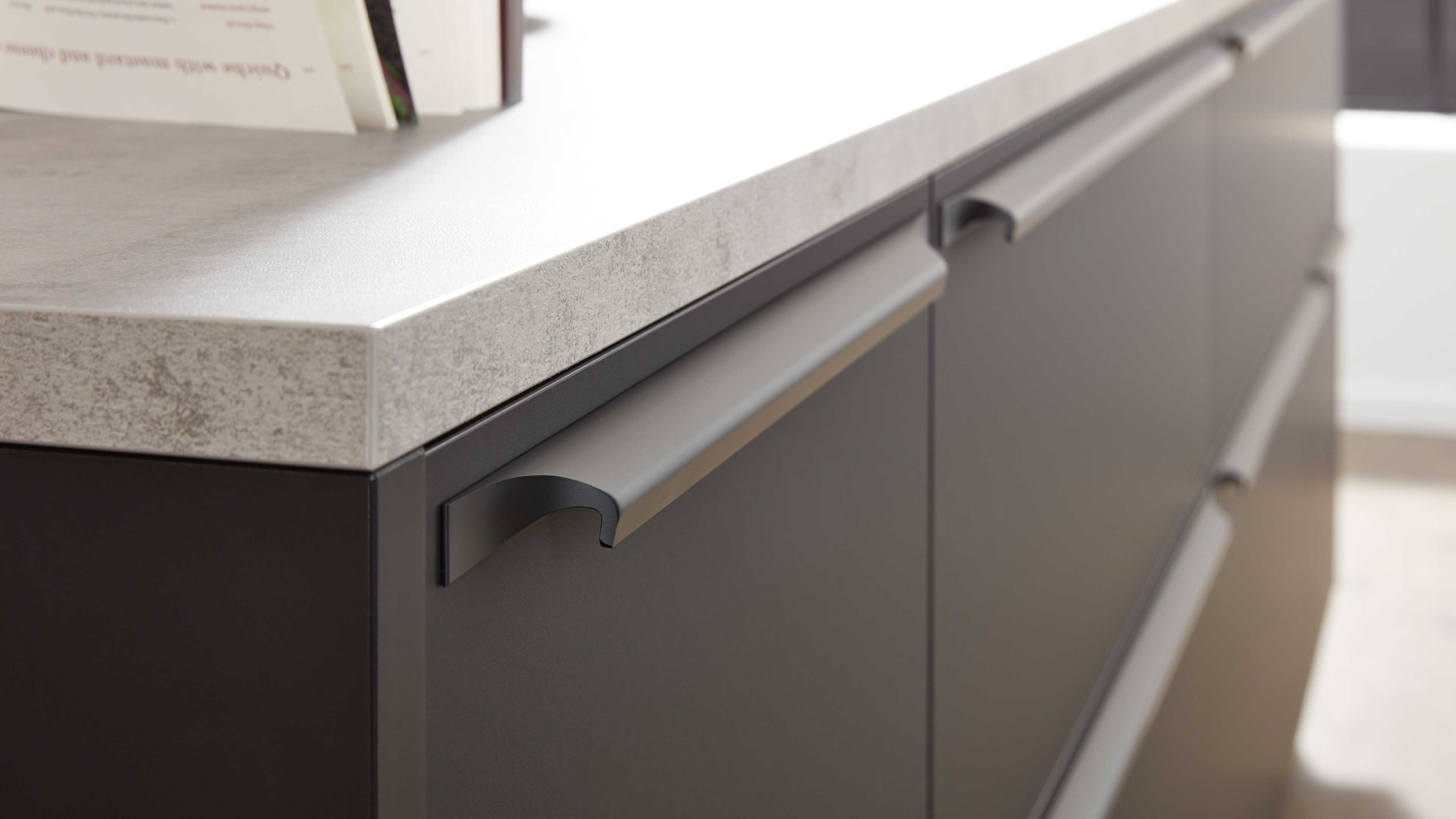 Front eines grauen Küchenunterschranks mit gebogenen Metallgriffen und hellgrauer, steinoptik-Arbeitsplatte.