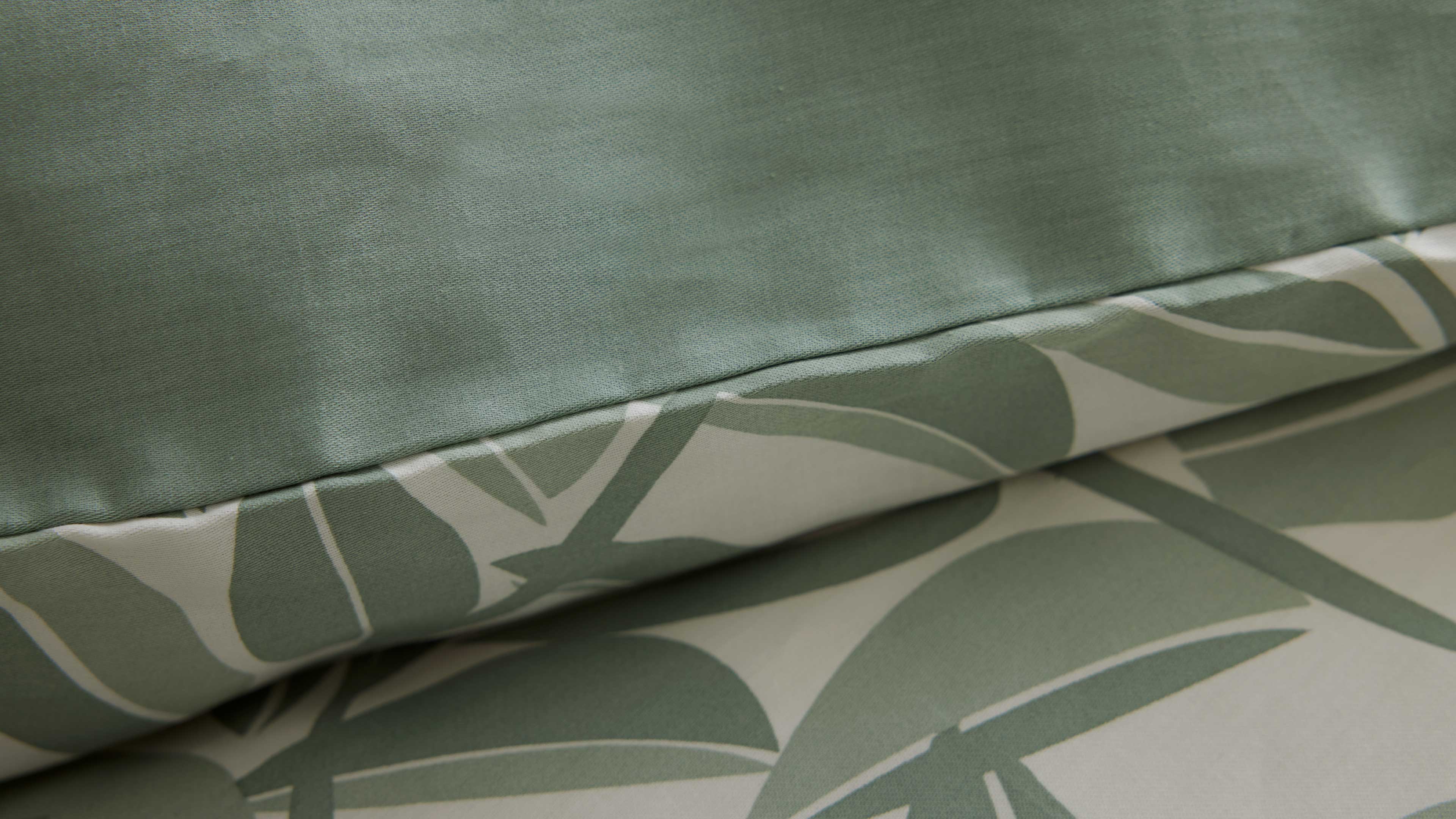 Nahaufnahme eines gepolsterten Kissens mit einfarbiger, leicht strukturierter grüner Oberseite und hellgrundigem Blattmuster an der Naht.