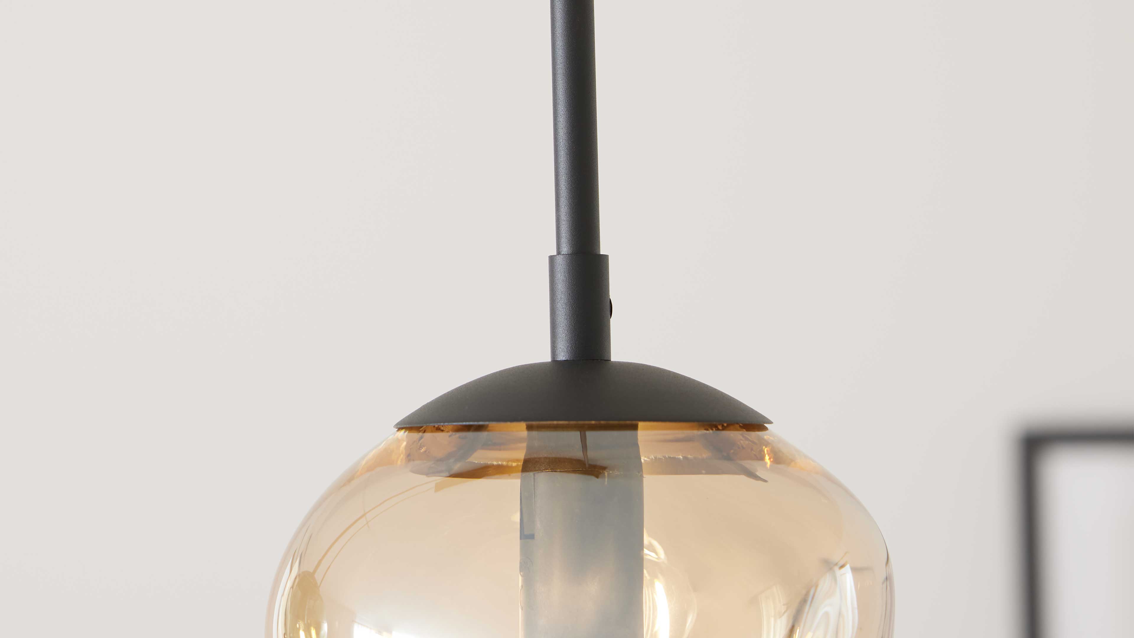 Hängelampe mit schwarzem Metallstiel und -schirm, halbtransparenter bernsteinfarbener Glaskugel und sichtbarer Glühbirne.