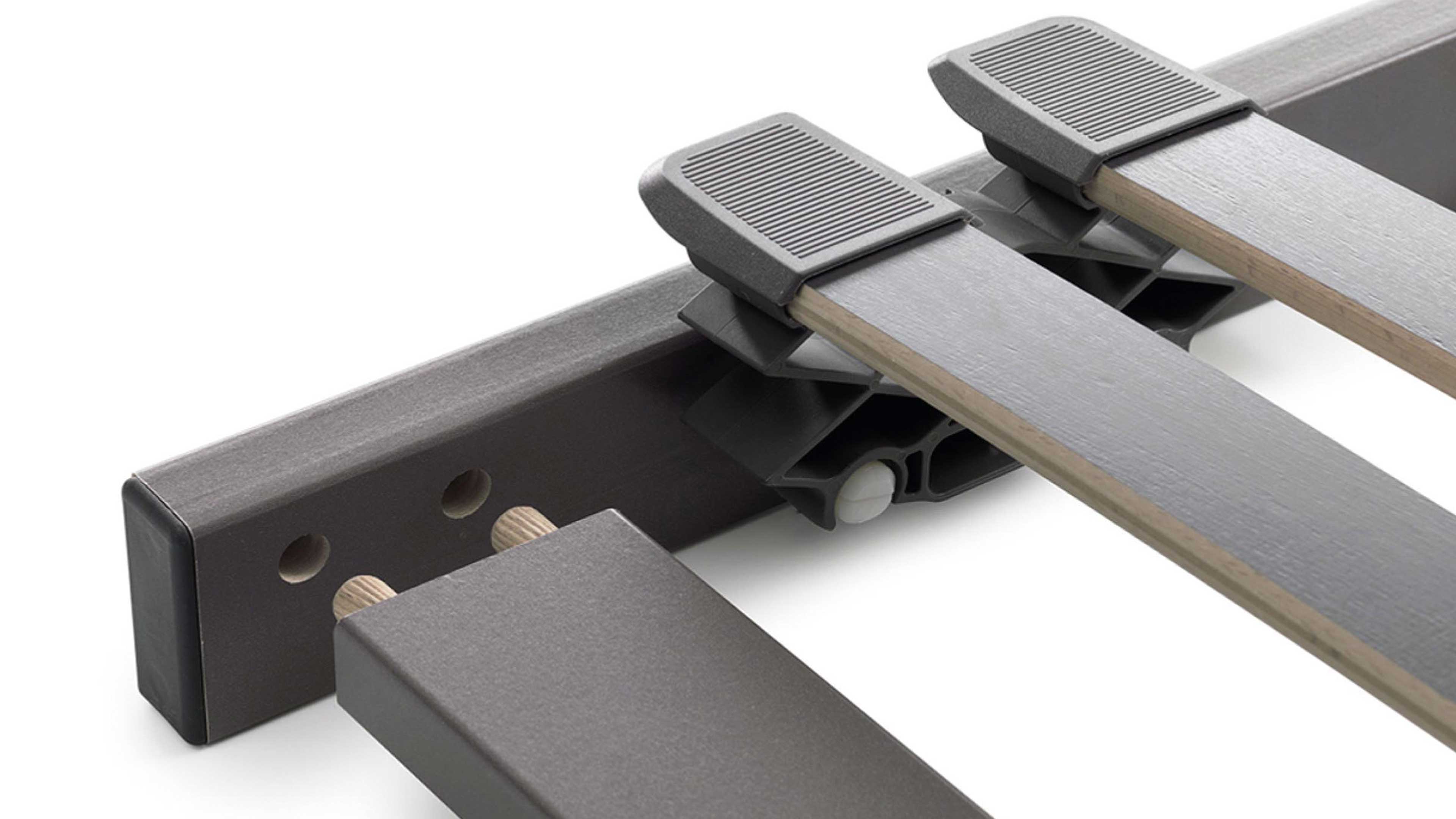 Lattenrost-Ausschnitt mit zwei grauen Holzlatten in grauen Kunststoffhaltern, gummiartige Auflagen und Querholm mit sichtbaren Holzdübeln.