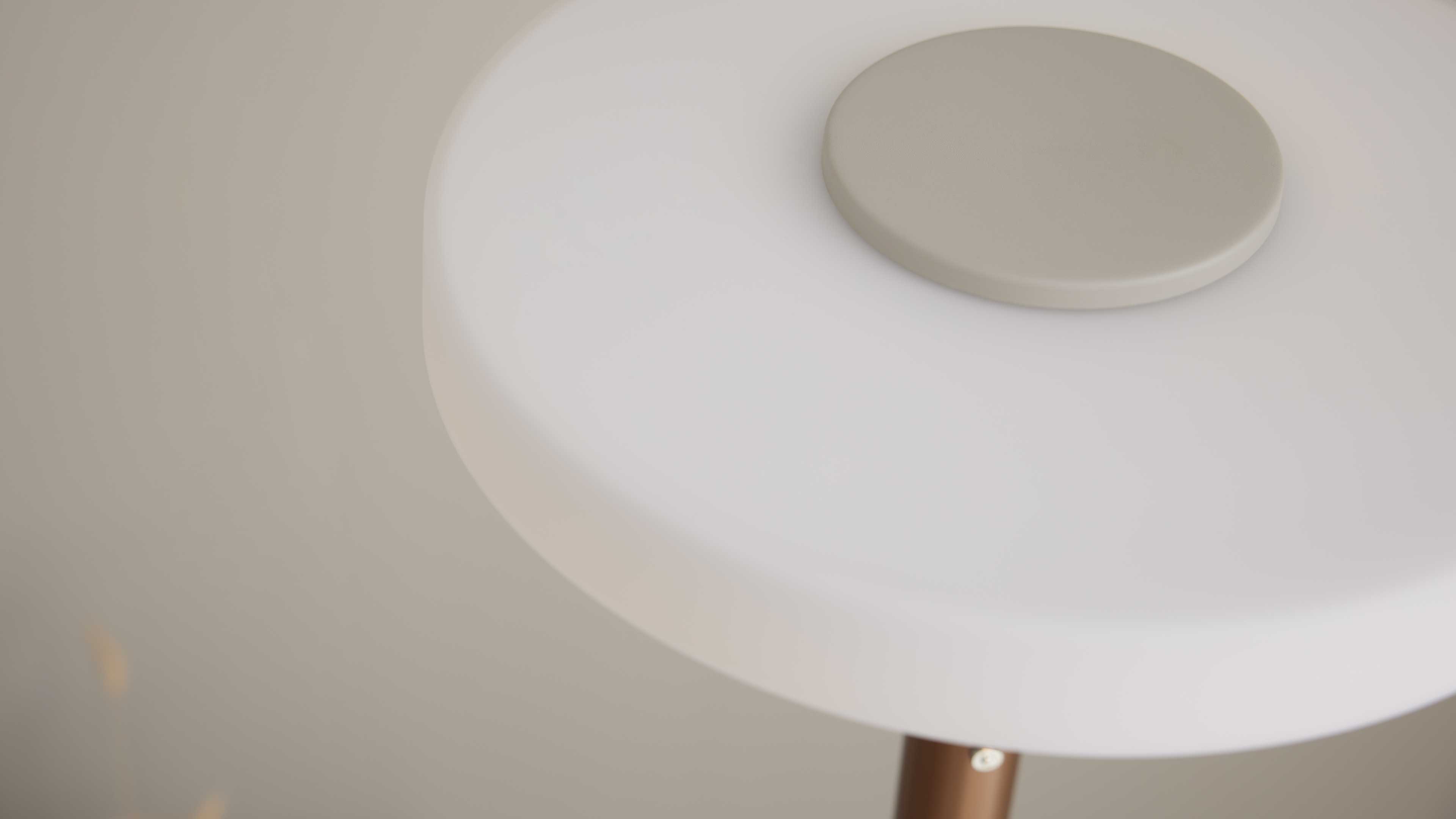 Runde weiße Tischplatte mit aufliegender runder beiger Ablage und sichtbarem bronzefarbenen Tischbein.