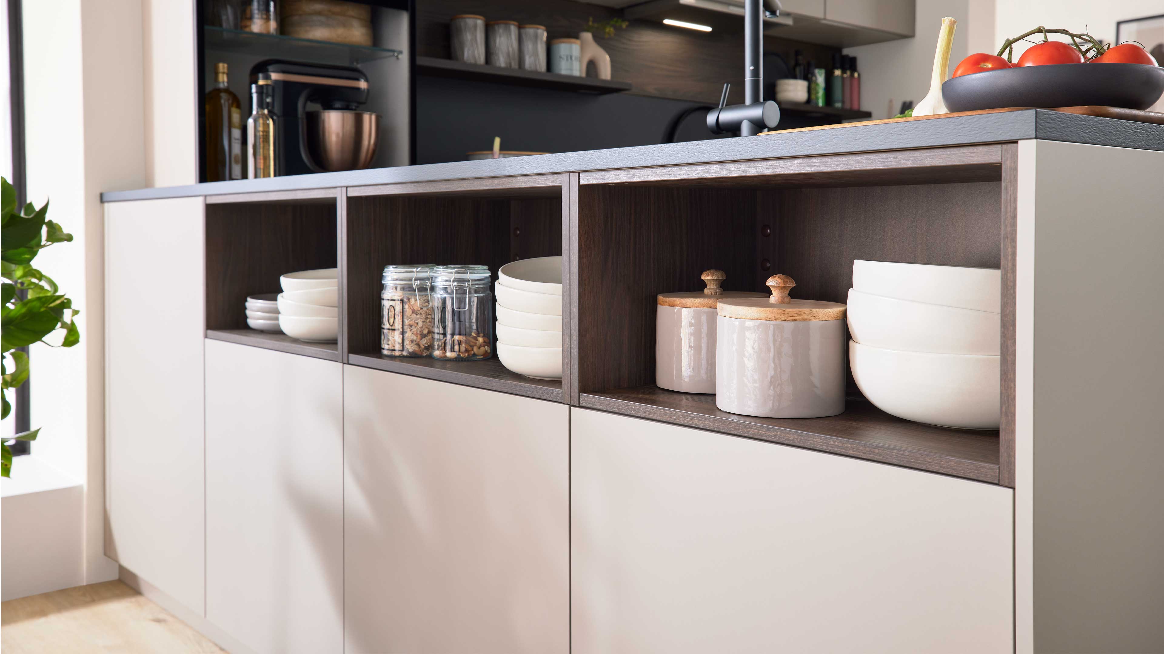 Niedrige Küchenzeile mit drei offenen Fächern, darin gestapelte weiße Schalen, Vorratsgläser und Keramikdosen mit Holzdeckeln.
