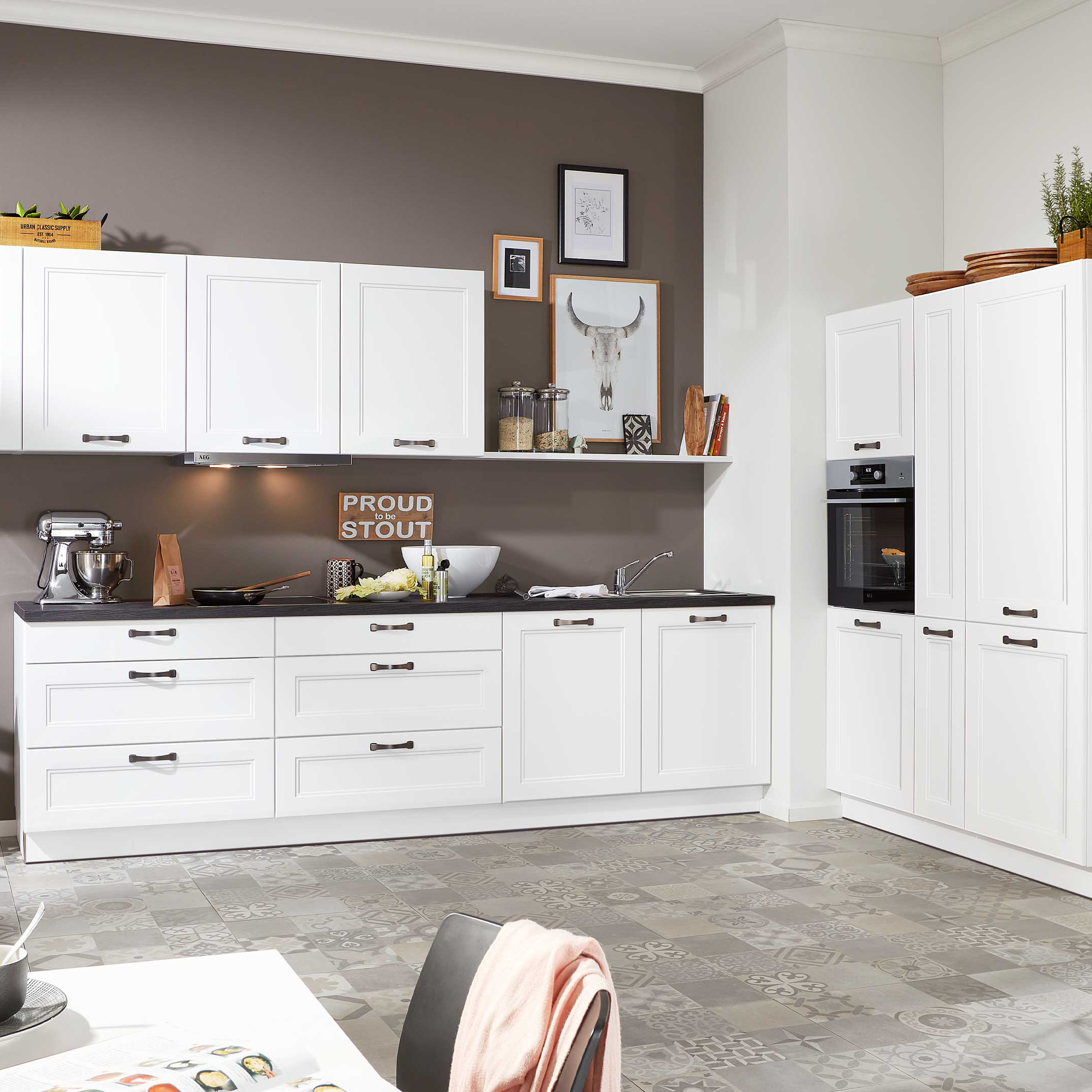 Weiße Küchenzeile mit durchgehender Arbeitsplatte in Dunkelgrau, Oberschränken mit Glasfront, Hochschrank mit Backofen und gemustertem Boden.