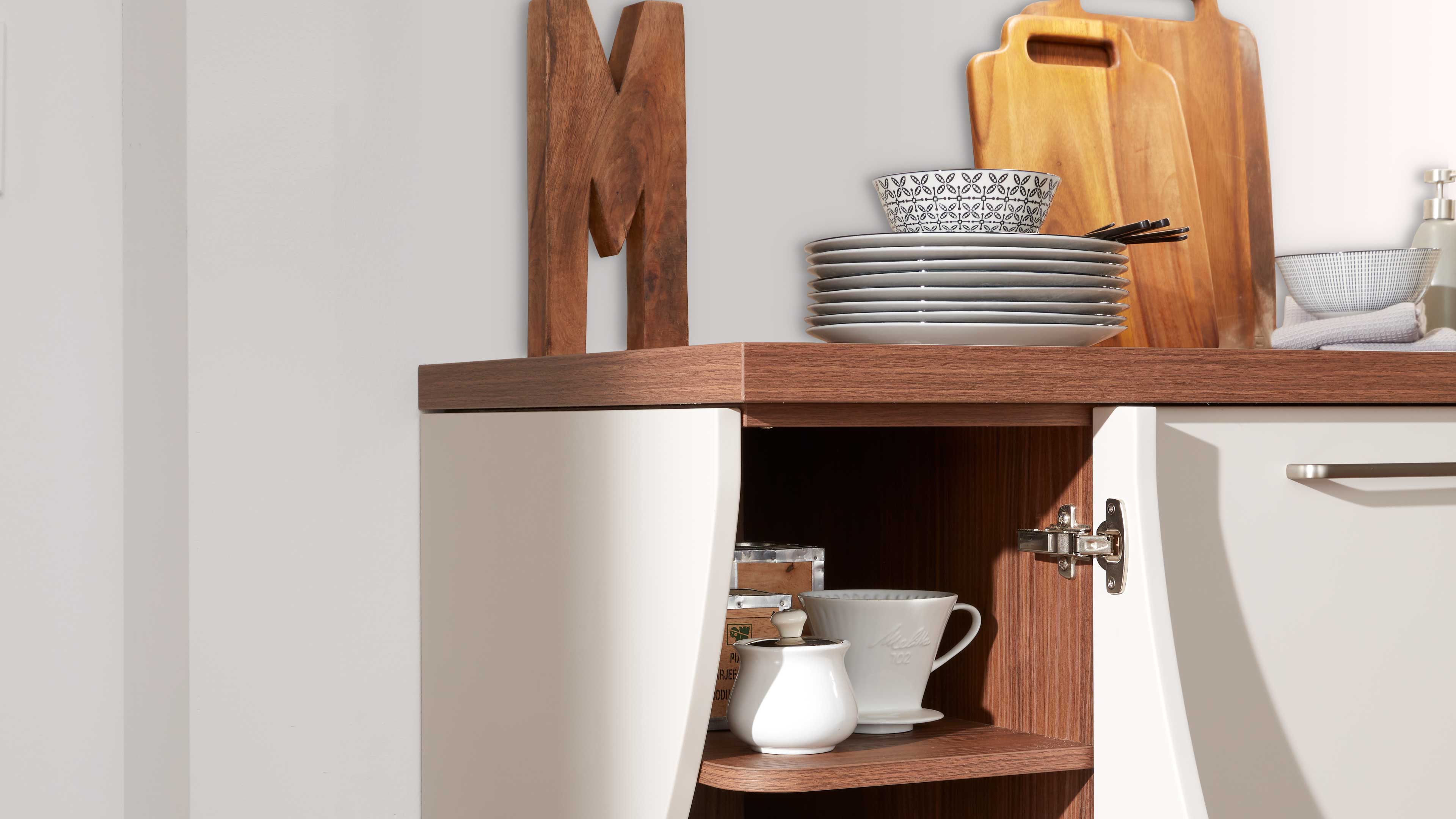 Offenes Küchenunterschrank-Eckmodul mit weißen, leicht geschwungenen Fronten, holzfarbener Arbeitsplatte und innen Holzoptik.