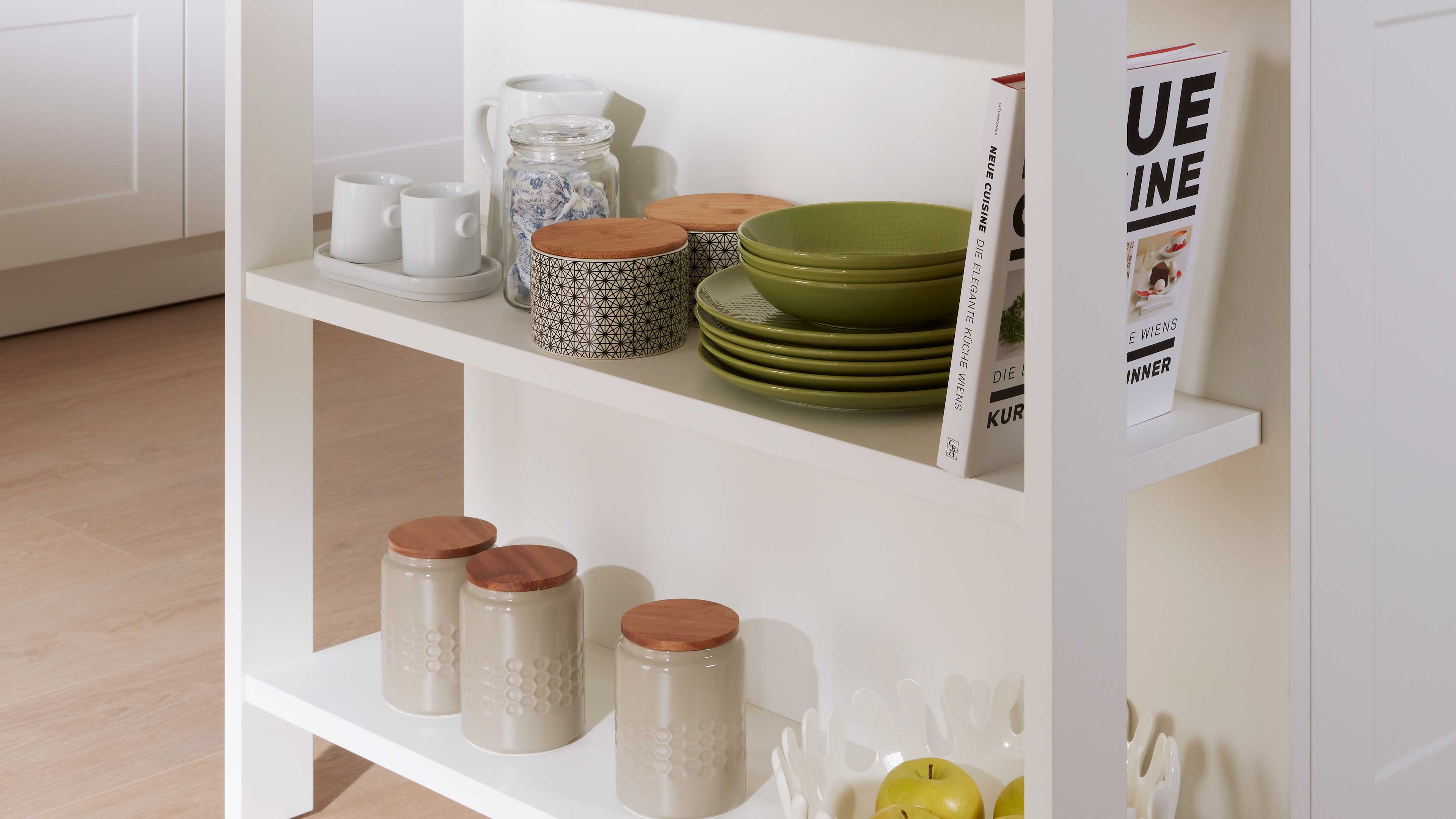 Weißes offenes Regal mit gestapelten olivgrünen Schalen und Tellern, gemusterten Vorratsdosen mit Holzdeckeln, Keramikbechern.