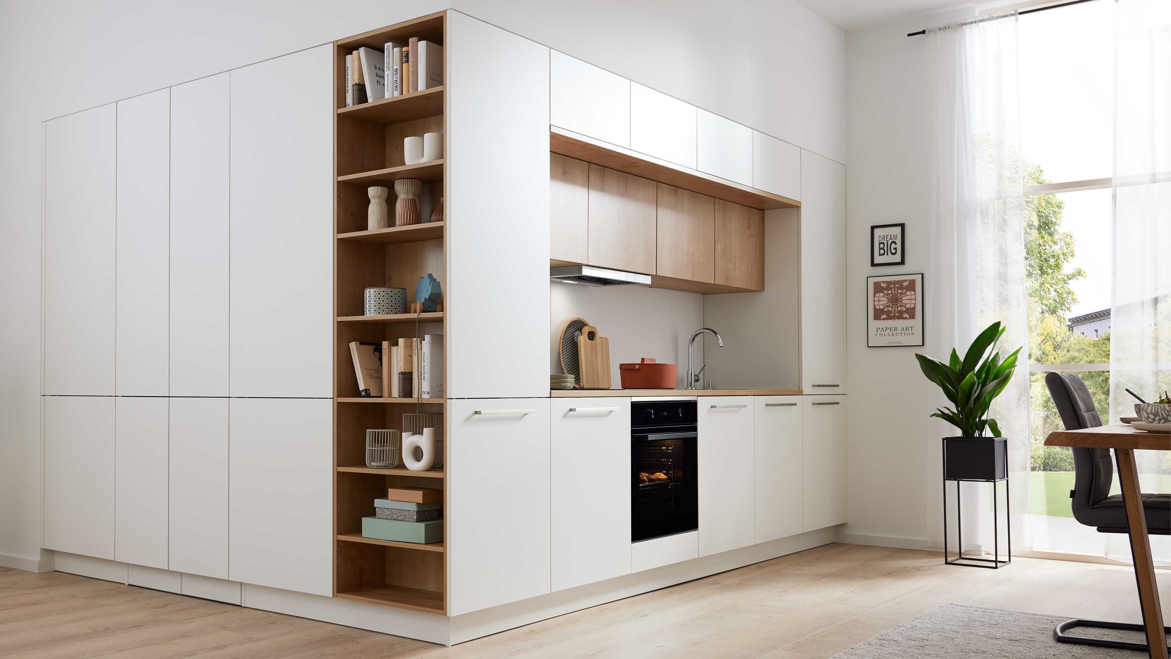 Weiße Küchenzeile mit Holzarbeitsfläche und offenen Regalfächern, mit Backofen, Spüle und Dunstabzug, daneben Pflanze am Fenster.