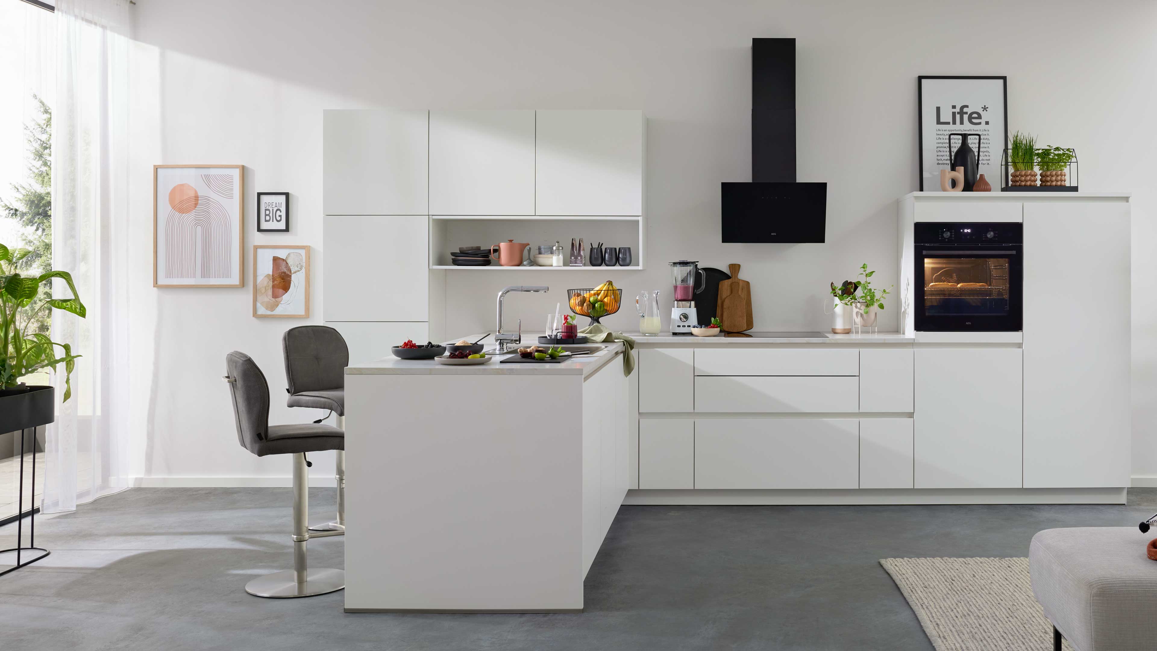 Weiße Kücheninsel mit Spüle, zwei graue Barhocker, weiße Hängeschränke, schwarzer Dunstabzug und eingebauter Ofen.