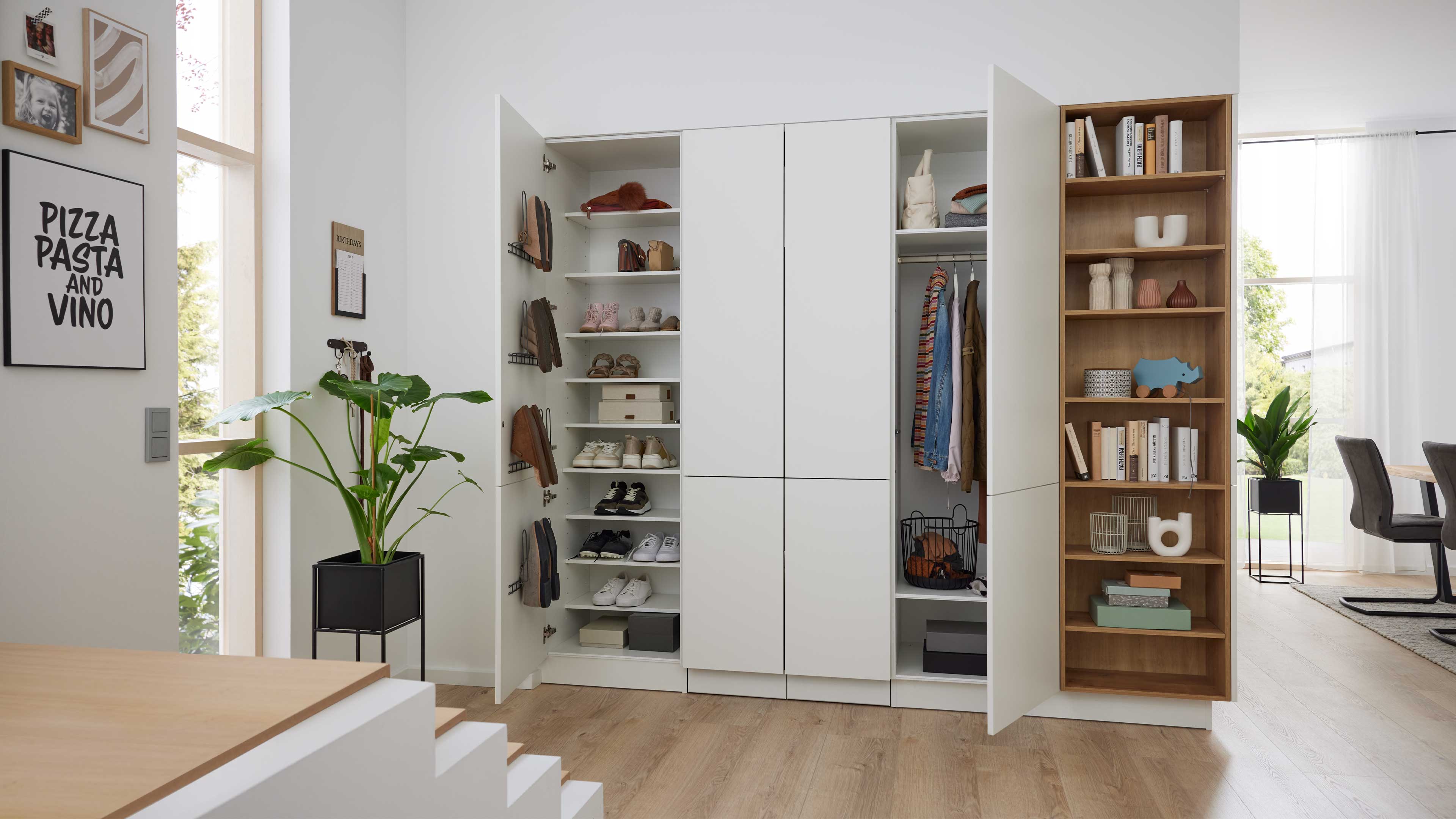 Weißer Garderobenschrank mit offenen Türen: Schuhregale links, Kleiderstange und Körbe mittig, rechts offenes Holzregal mit Büchern und Deko.