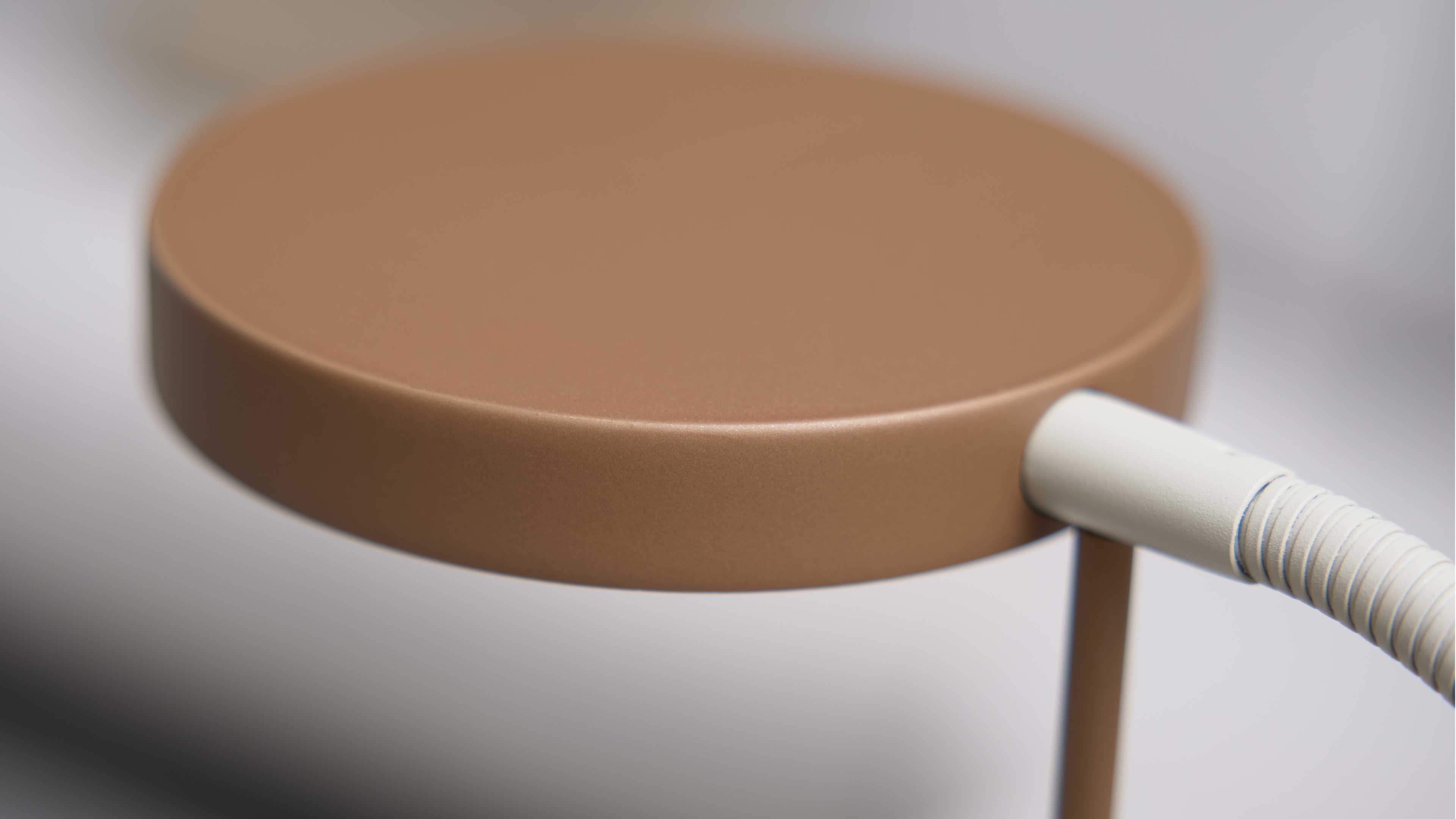 Rundes, flaches Lampenschirm-Element in mattbraun in Nahaufnahme, rechts ein weiß geriffelter flexibler Anschluss und ein dünner Ständer.