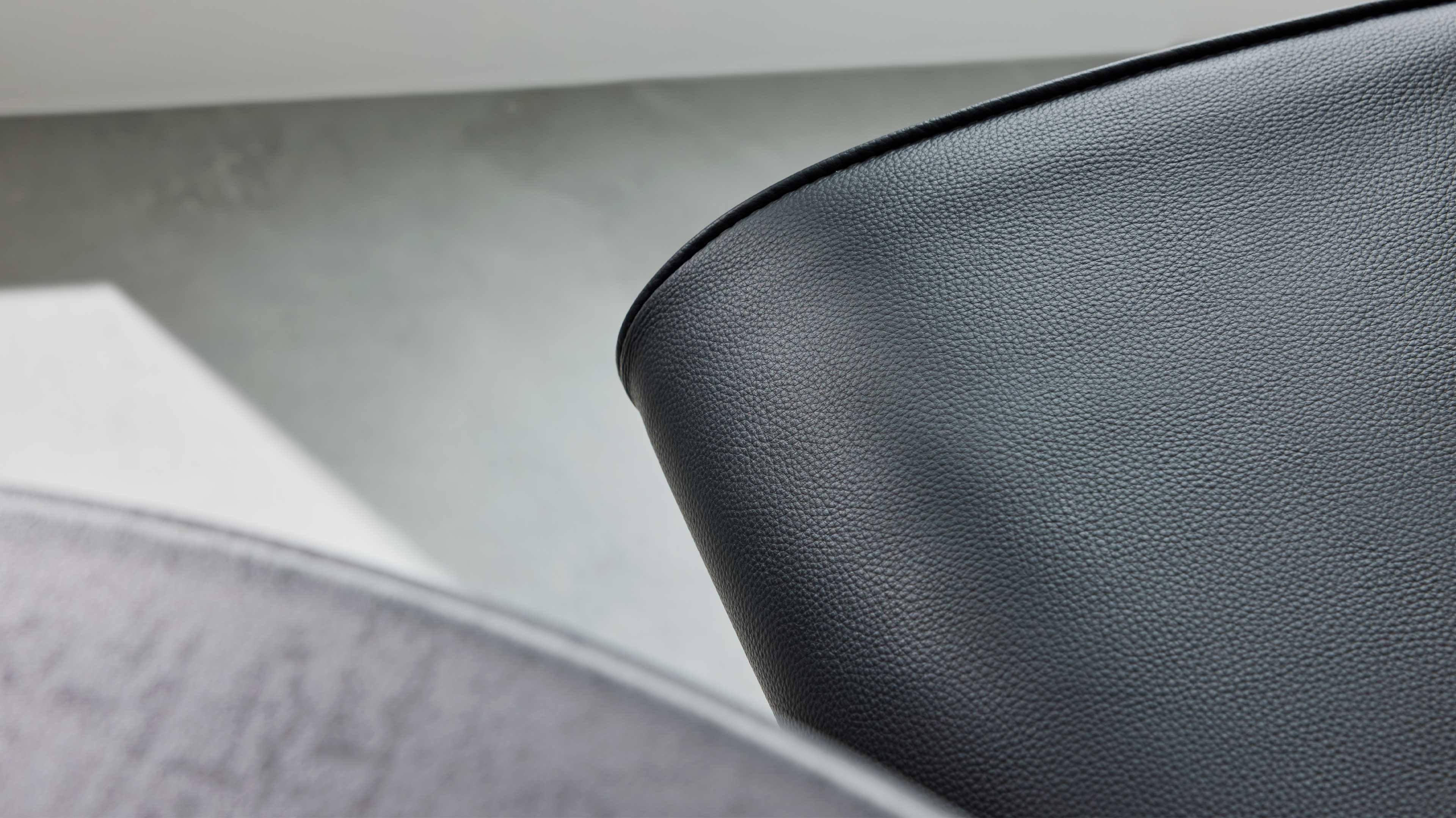 Nahaufnahme der abgerundeten Rückenlehne eines schwarzen, fein genarbten Stuhlbezugs, links angeschnittene graue Polsterfläche sichtbar.