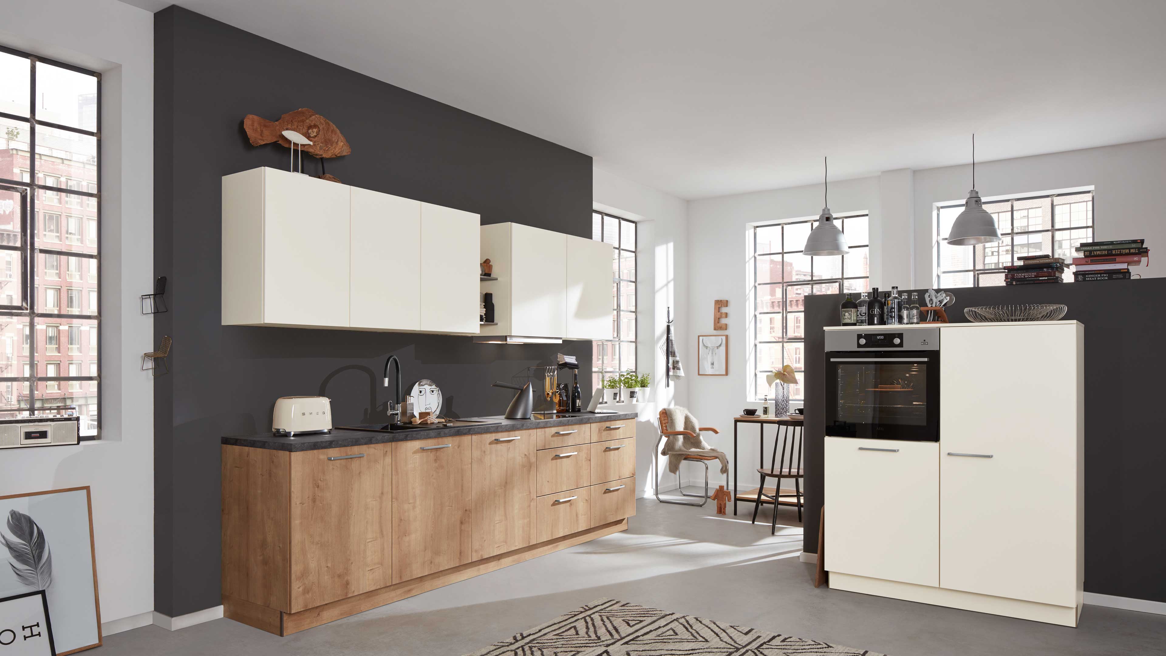 Küche mit Unterschränken in Holzoptik, cremefarbenen Hängeschränken, dunkler Arbeitsplatte und integriertem Backofen im Hochschrank.