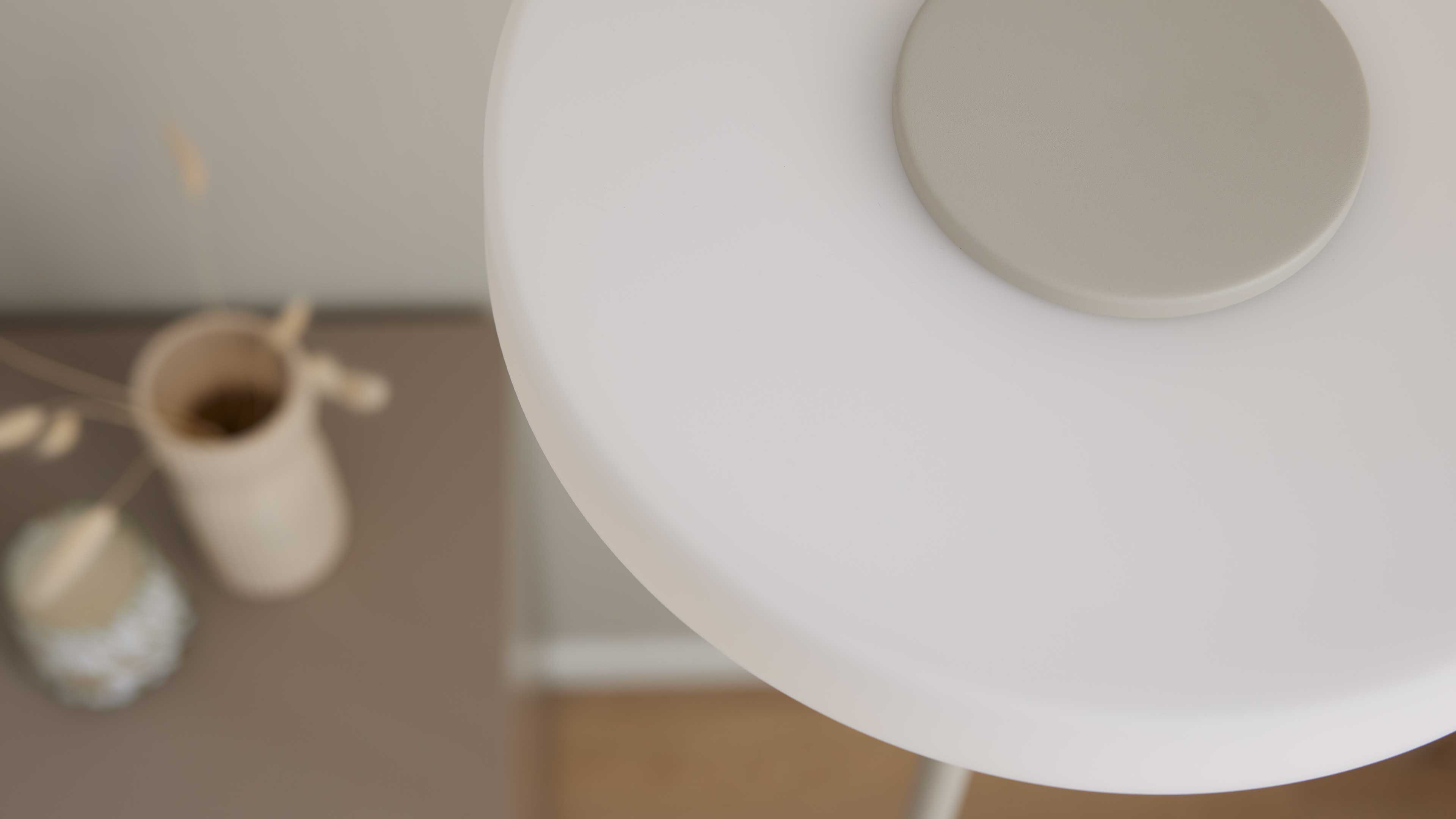 Große weiße runde Fläche mit rundem hellgrauen Einsatz oben rechts, im unscharfen Hintergrund ein Tisch mit beigen Vasen.