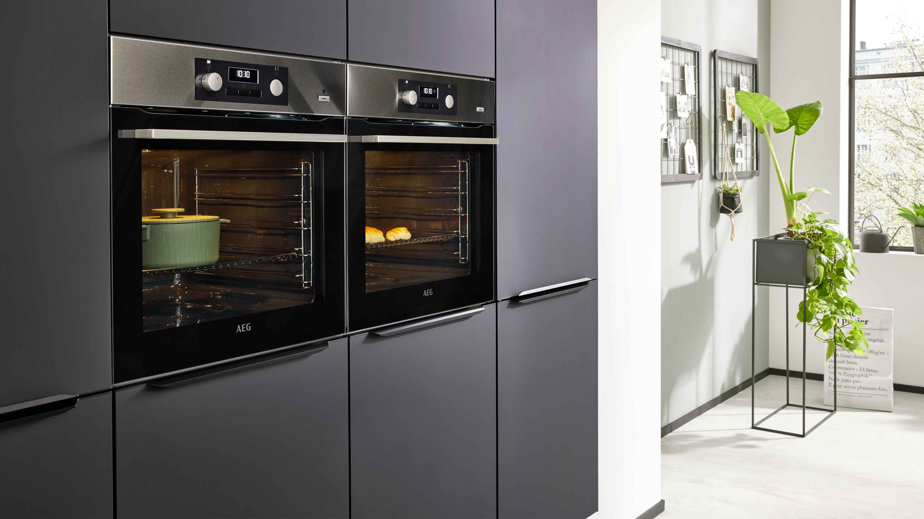 Zwei eingebaute schwarze Backöfen in grauer Küchenzeile, links ein grüner Topf im Innenraum, rechts zwei Brötchen auf dem Rost.