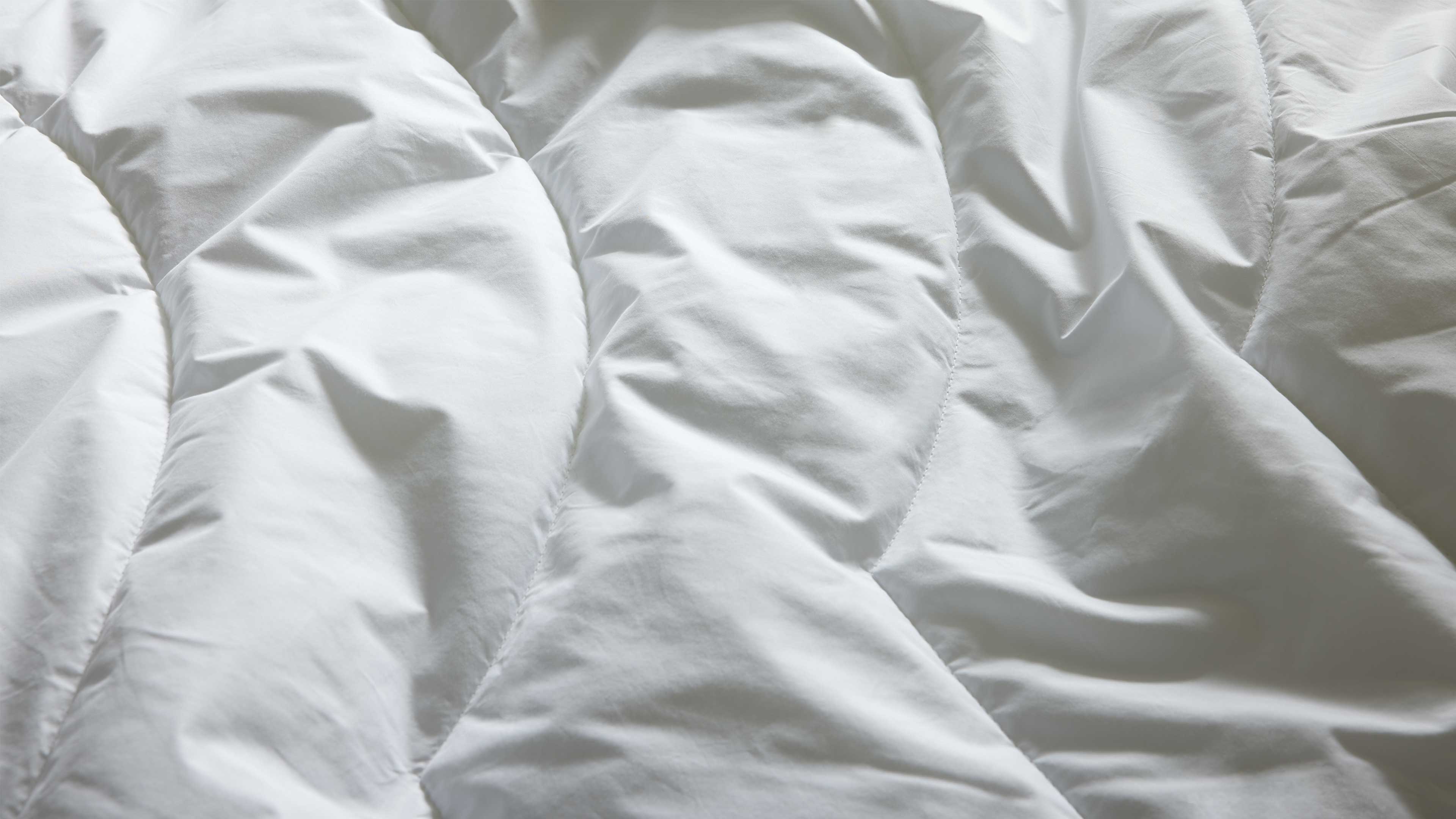 Nahaufnahme einer weißen gesteppten Bettdecke mit breiten geschwungenen Steppnähten, Wattung und sichtbaren Falten.