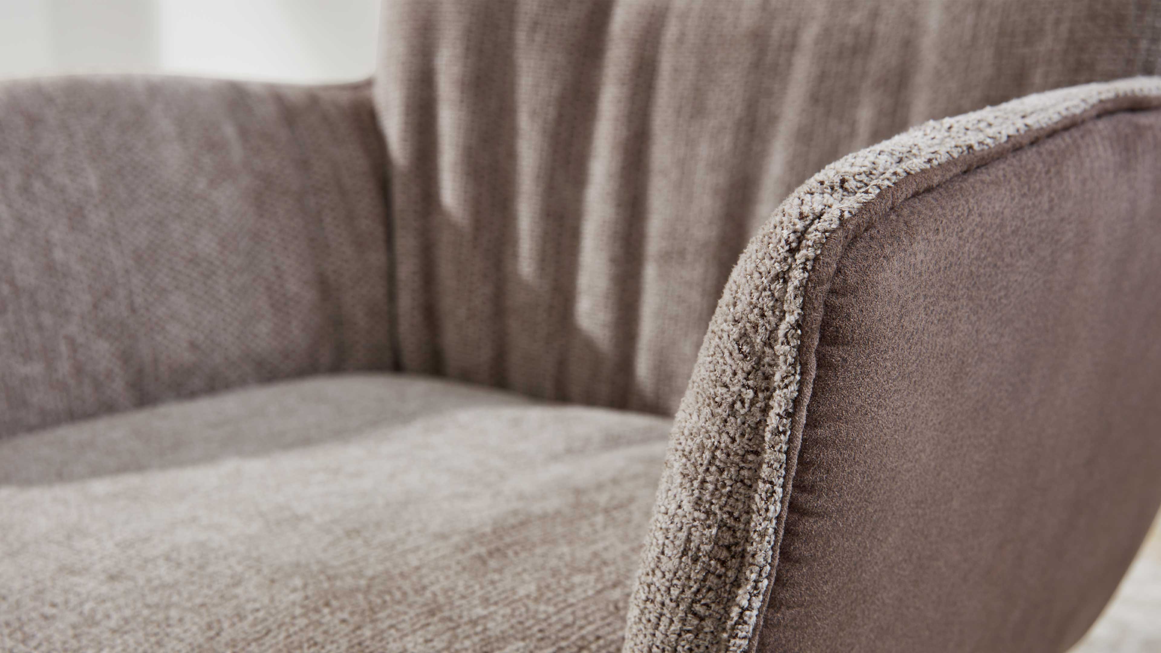 Nahaufnahme eines hellbraunen Polstersessels mit abgerundetem Armteil, Struktur des Bezugs und flauschigem Besatz an der Kante.