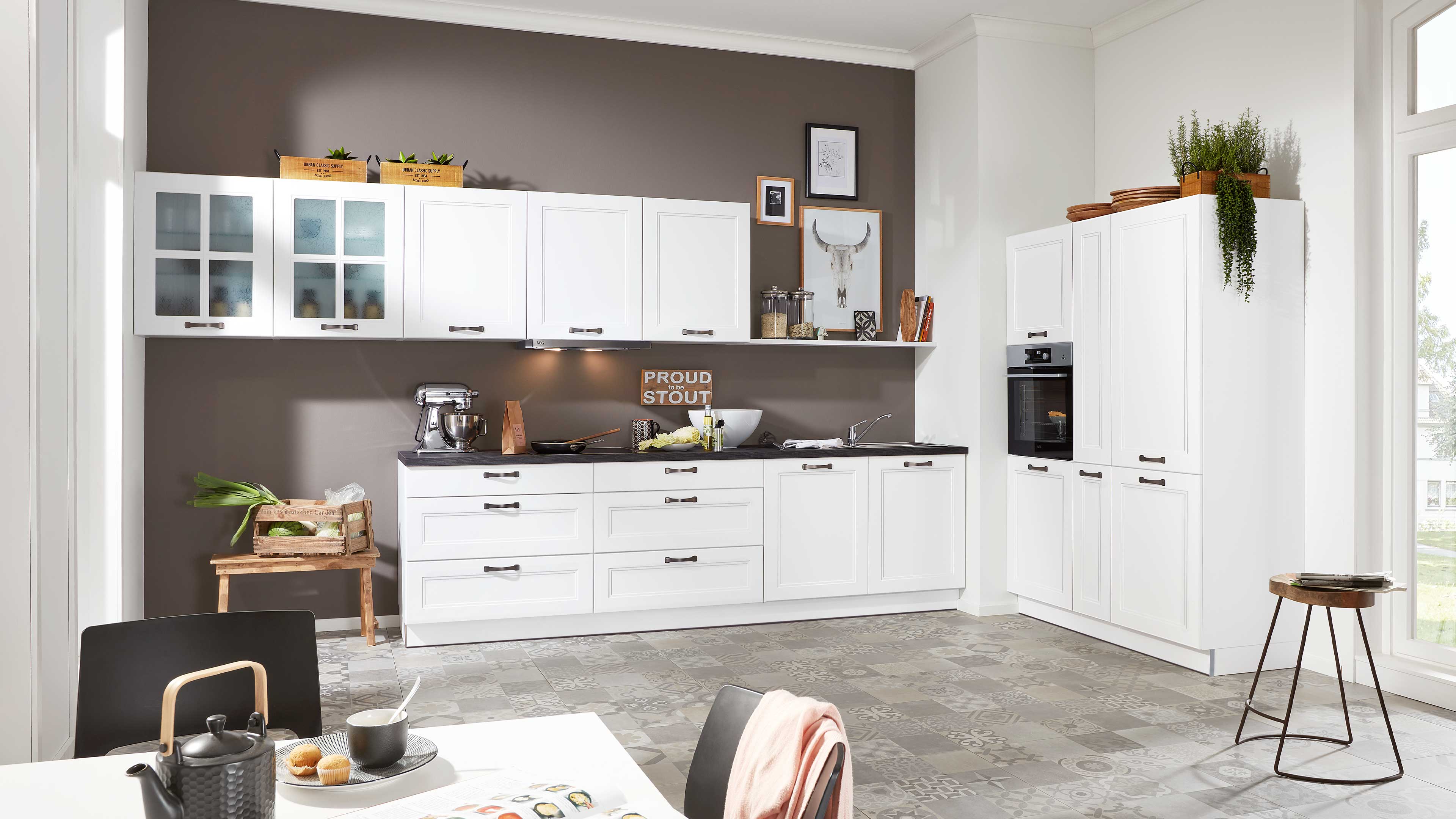 Weiße Küchenzeile mit durchgehender Arbeitsplatte in Dunkelgrau, Oberschränken mit Glasfront, Hochschrank mit Backofen und gemustertem Boden.