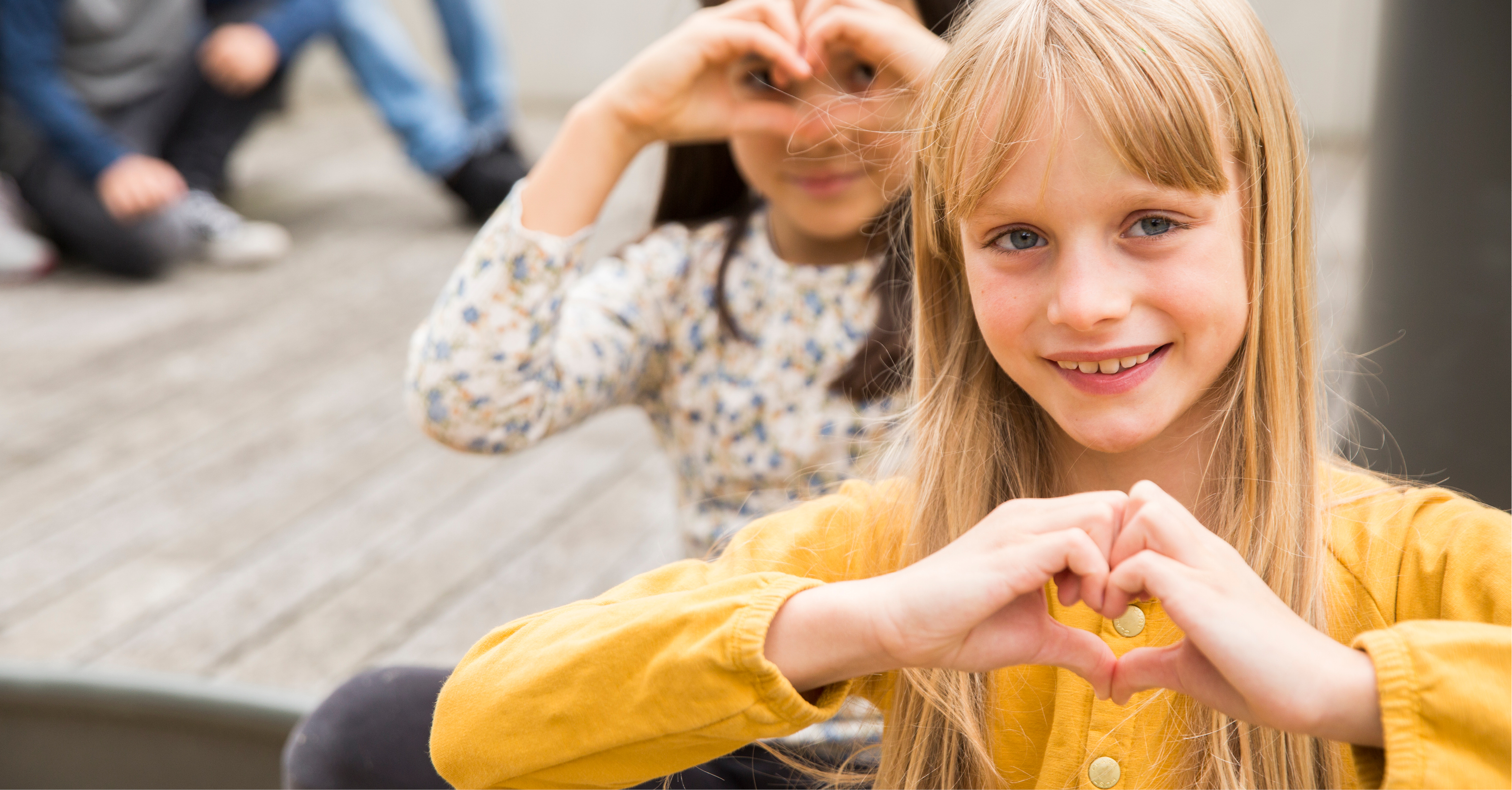 Zwei Kinder von SOS Kinderdorf zeigen mit Händen geformte Herzen