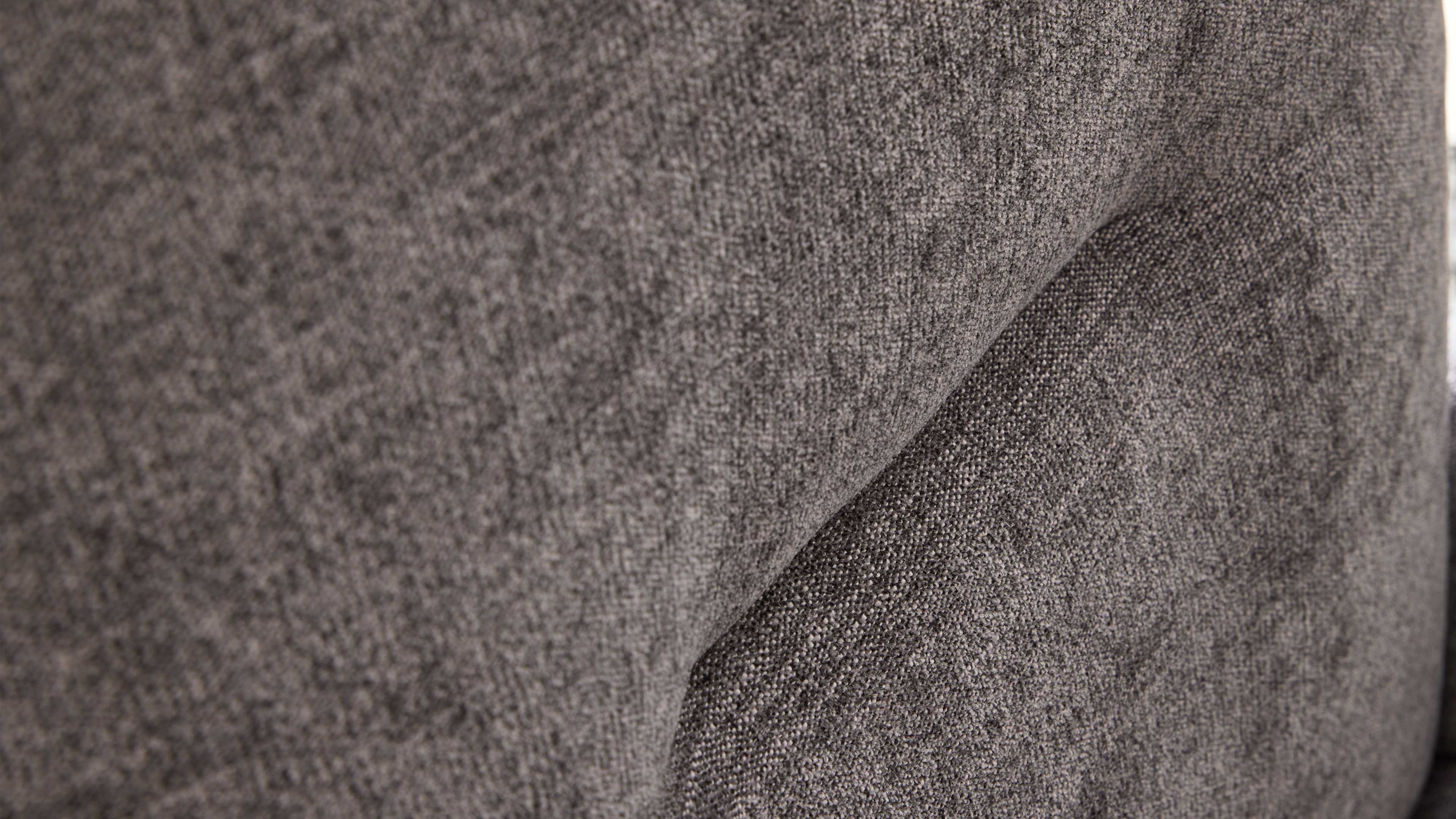 Nahaufnahme eines grauen, strukturierten Polsterstoffs mit angedeuteter Falte und feiner, körniger Webstruktur.
