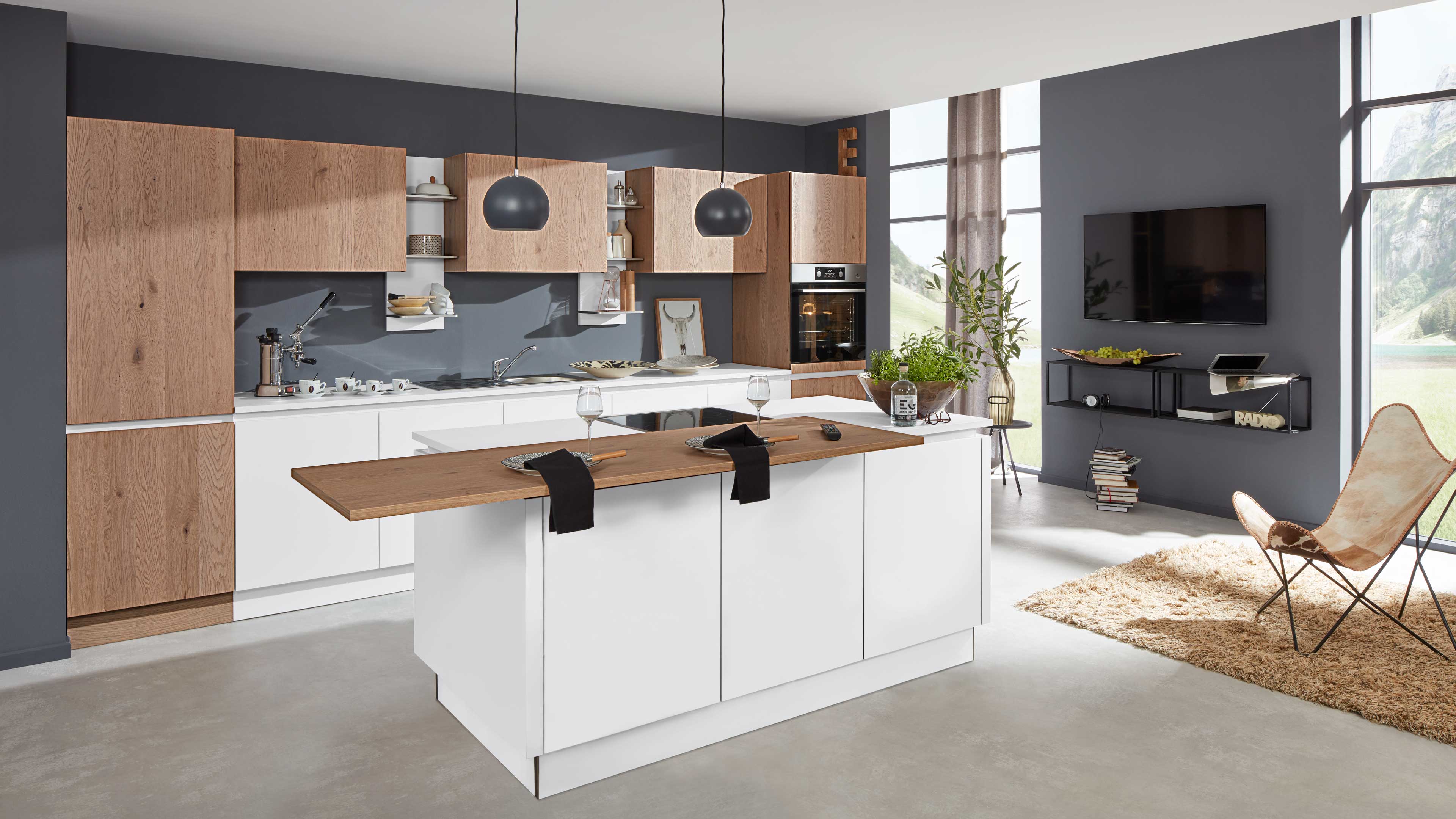 Offene Küche mit zentraler weißer Insel und aufgelegter Holzarbeitsplatte, Holz-Wandschränke in heller Eichenoptik und dunkler Wand.