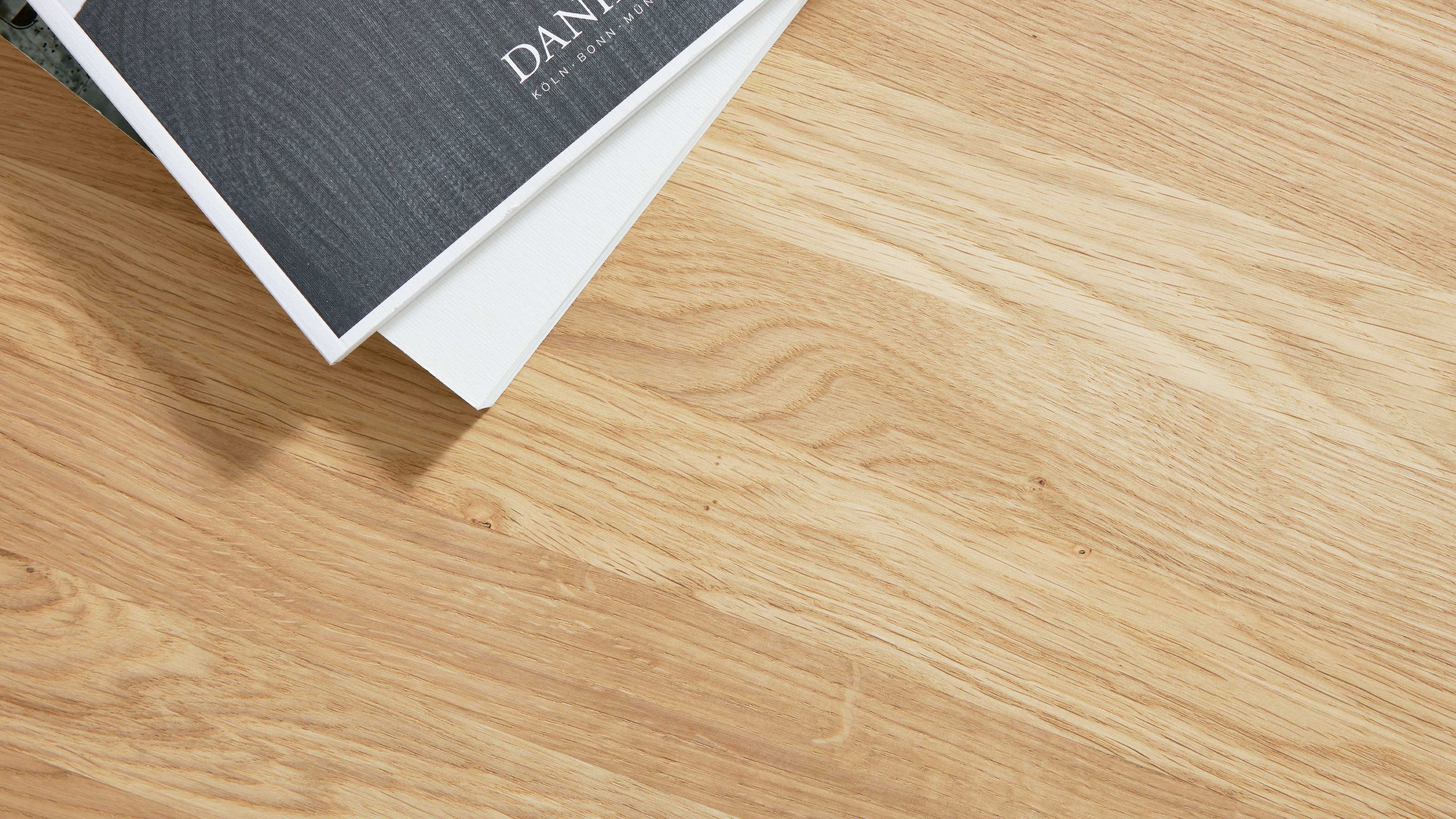 Helle Holz-Tischplatte mit sichtbarer Maserung, oben links zwei übereinanderliegende Bücher.