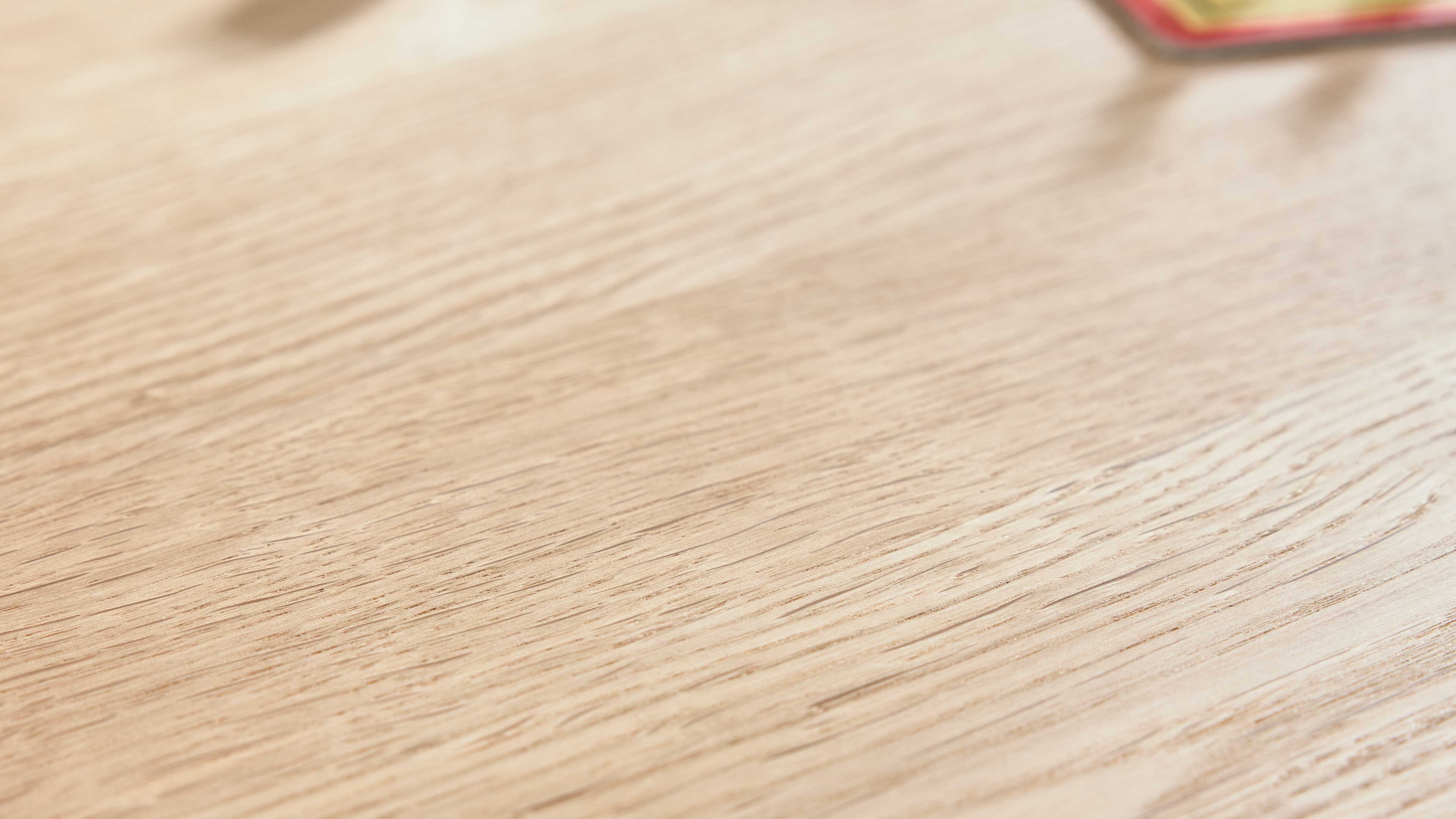 Helle Holzoberfläche mit markanter Längsmaserung, großflächig sichtbar, oben rechts ein unscharfer roter Rand eines Gegenstands.