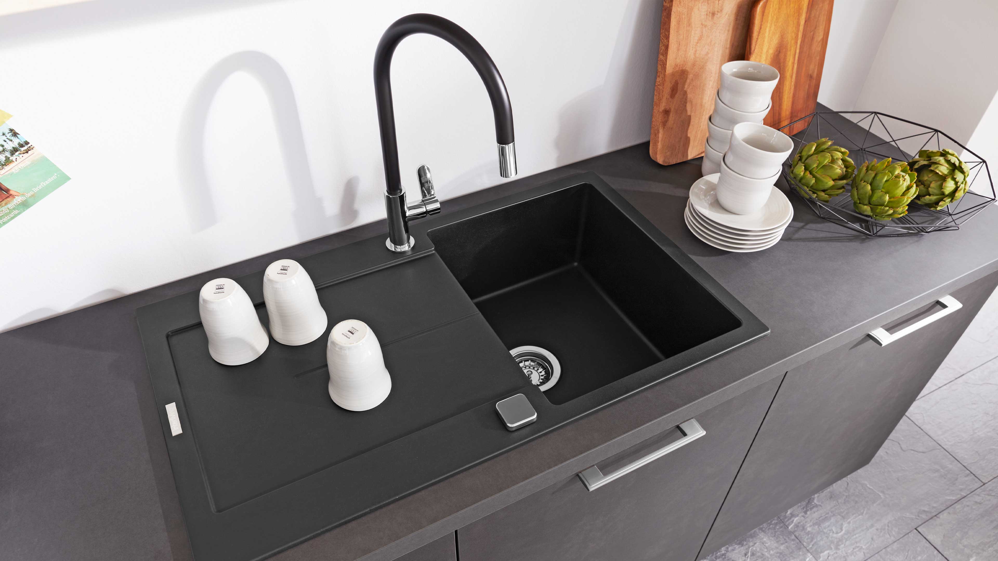 Matt-schwarze Einbauspüle mit rechteckigem Becken, integrierter Abtropffläche und gebogenem schwarzen Armaturhals mit Chromabschluss.