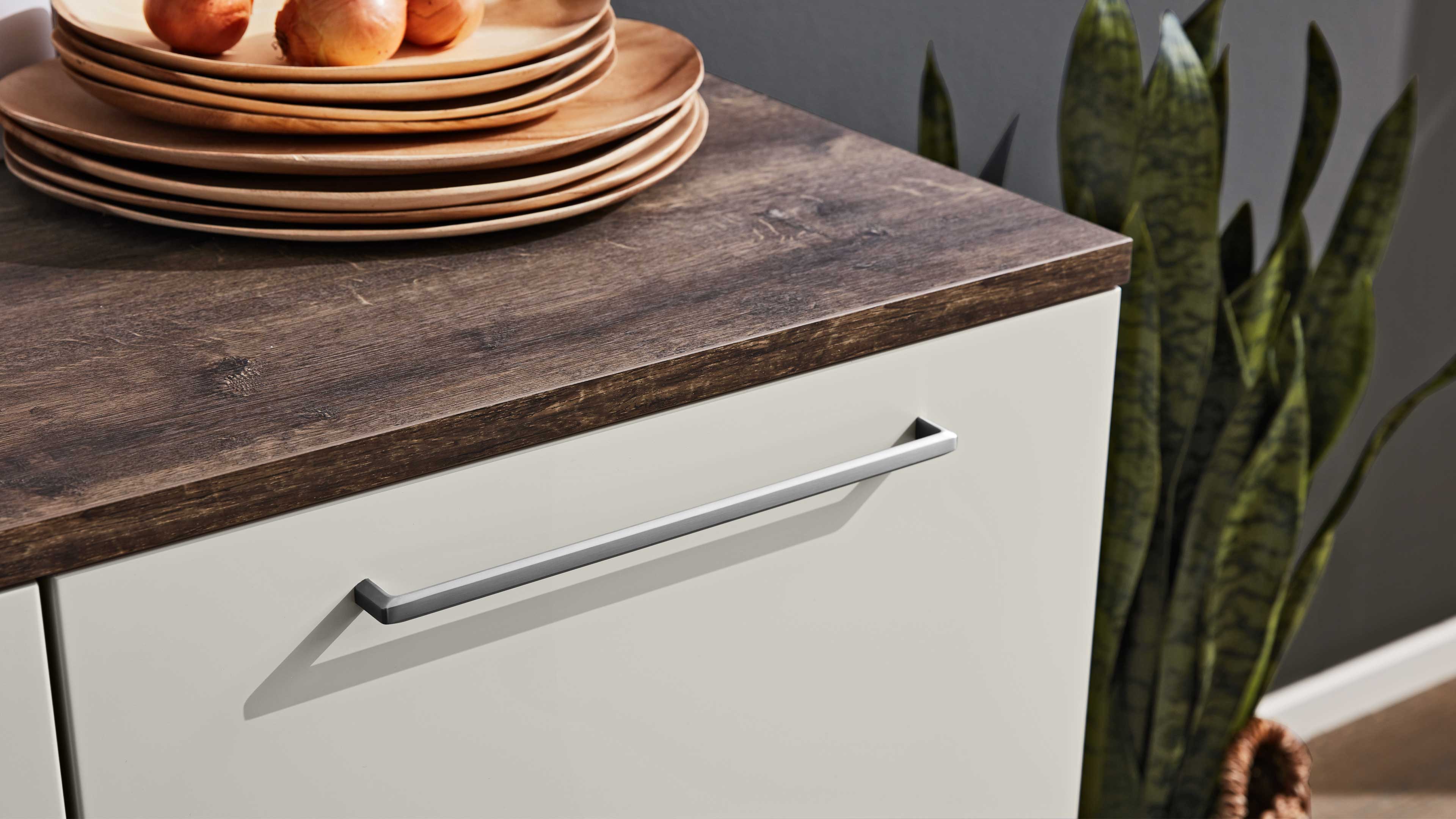 Schublade mit langem silbernem Griff unter dunkler Holzarbeitsplatte, oben gestapelte Holzplatten mit Zwiebeln.