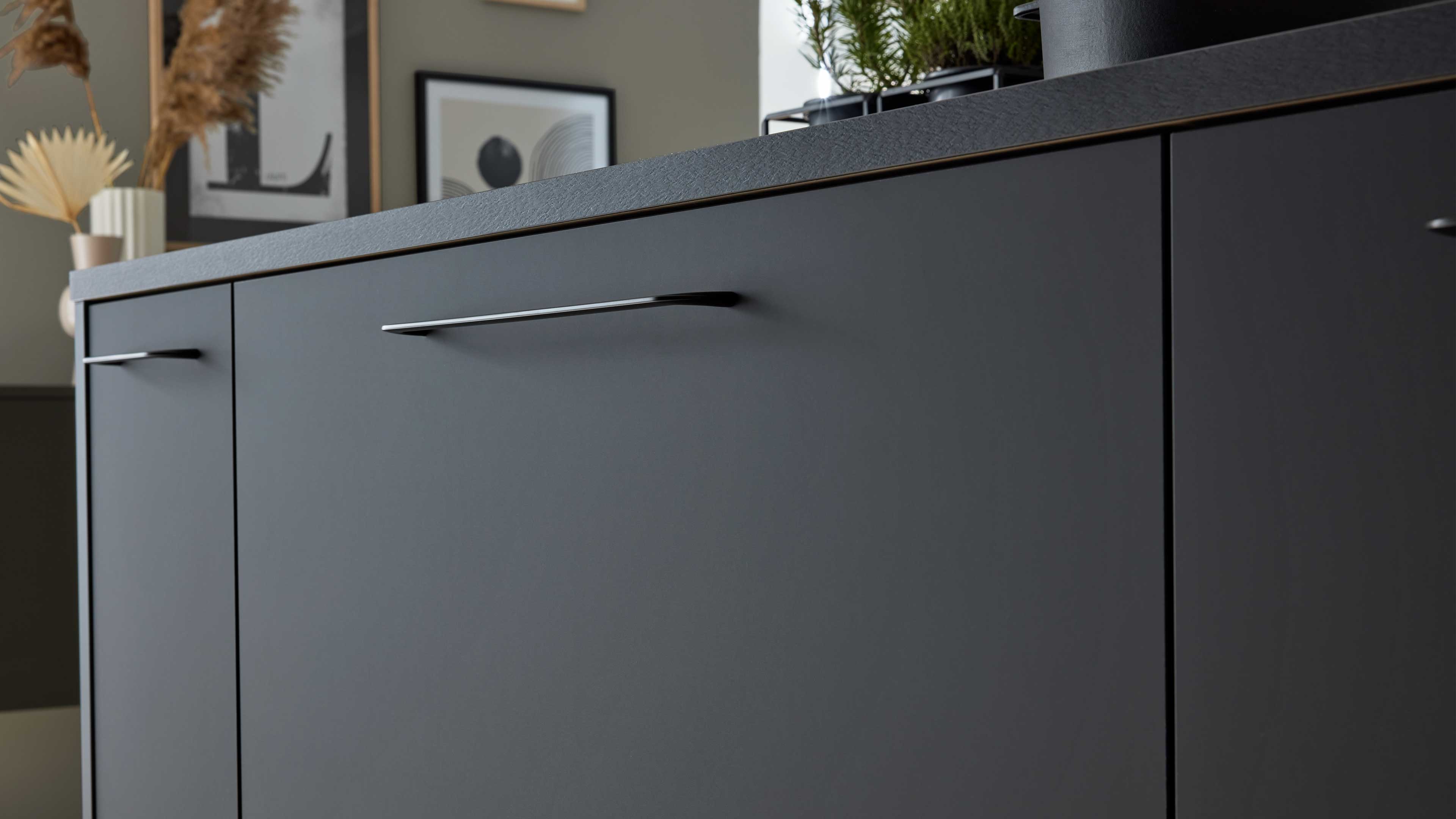 Dunkelgrauer Unterschrank mit mehreren flachen Türen und schlanken verchromten Griffen, leicht strukturierte Arbeitsplatte oben.