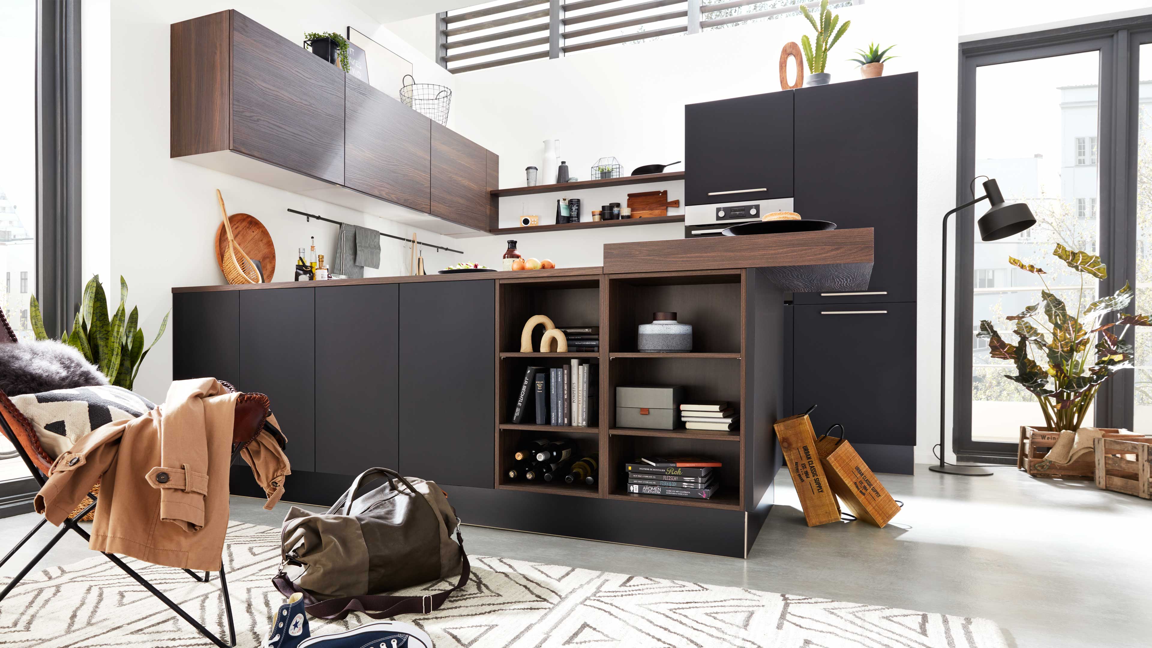 Dunkelgraue Küchenzeile mit Holzarbeitsplatte und offenen Regalfächern, hängenden Holzoberschränken, Pflanzen und Stuhl mit Jacke.