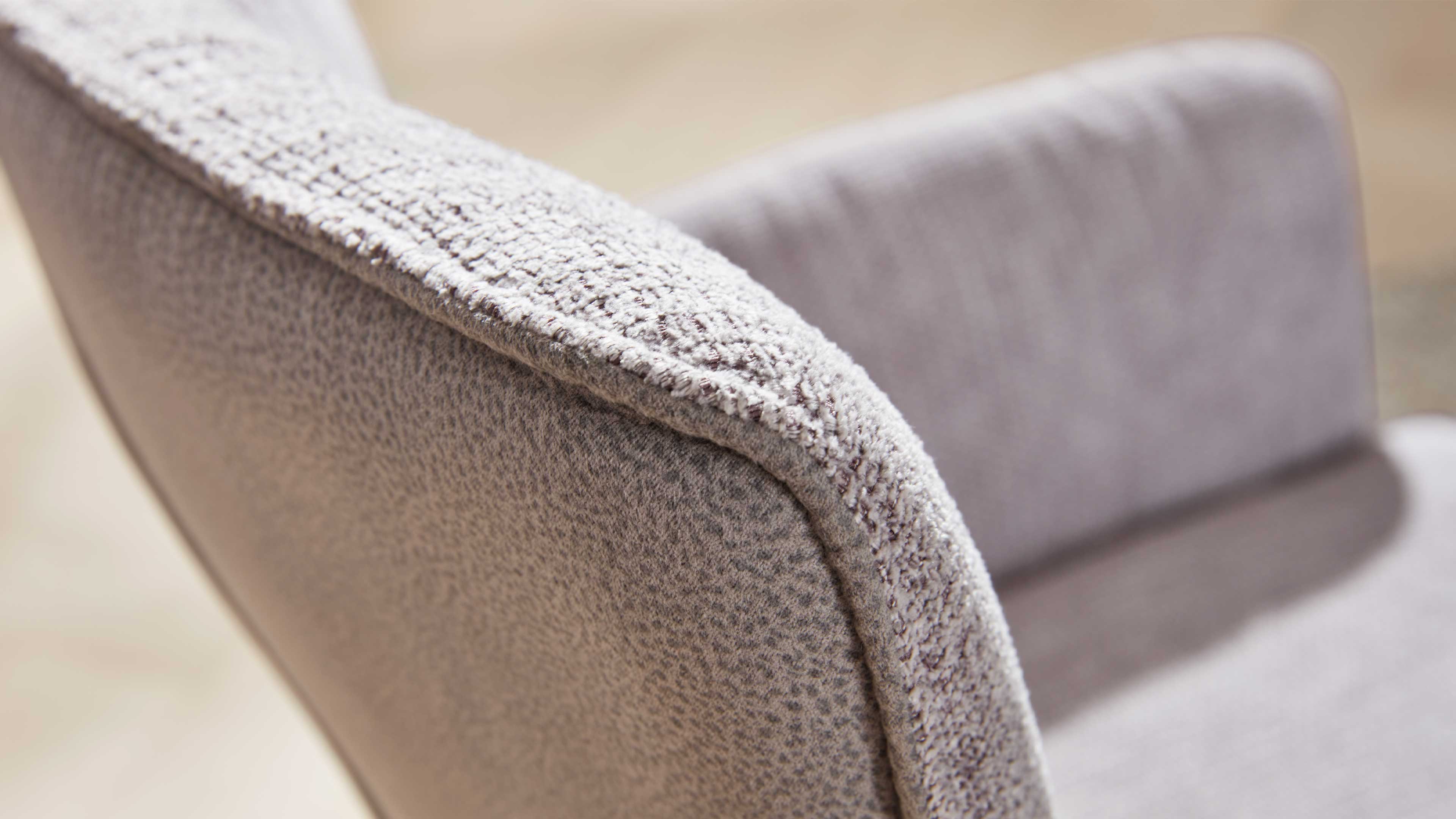 Nahaufnahme der gepolsterten Armlehne eines Stuhls mit hellgrauem, grobtexturiertem Stoff und sichtbarer Naht.