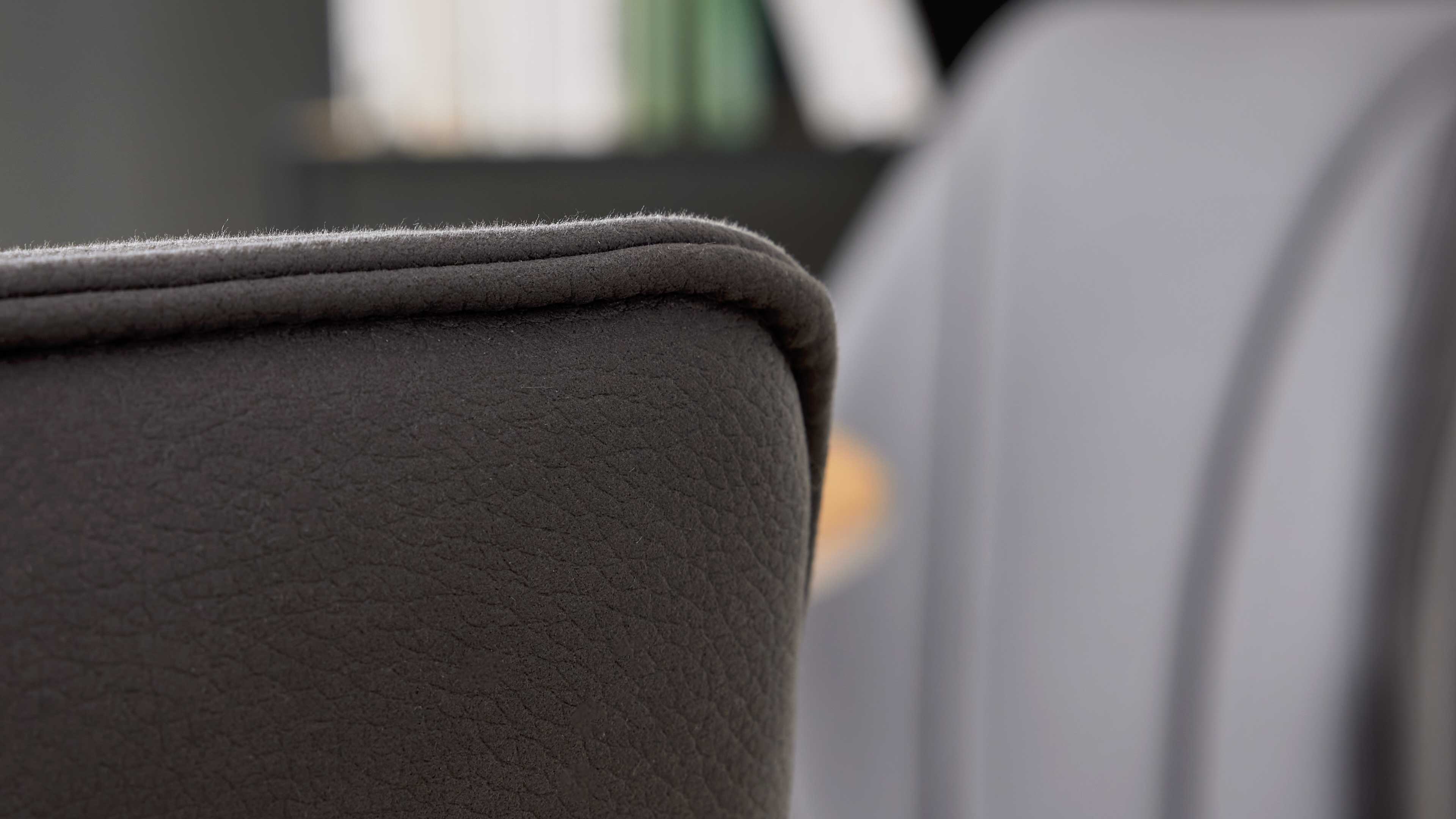 Nahaufnahme einer dunkelgrauen Polsterlehne mit sichtbarer Kedernaht und feiner Lederstruktur, unscharfer Hintergrund.