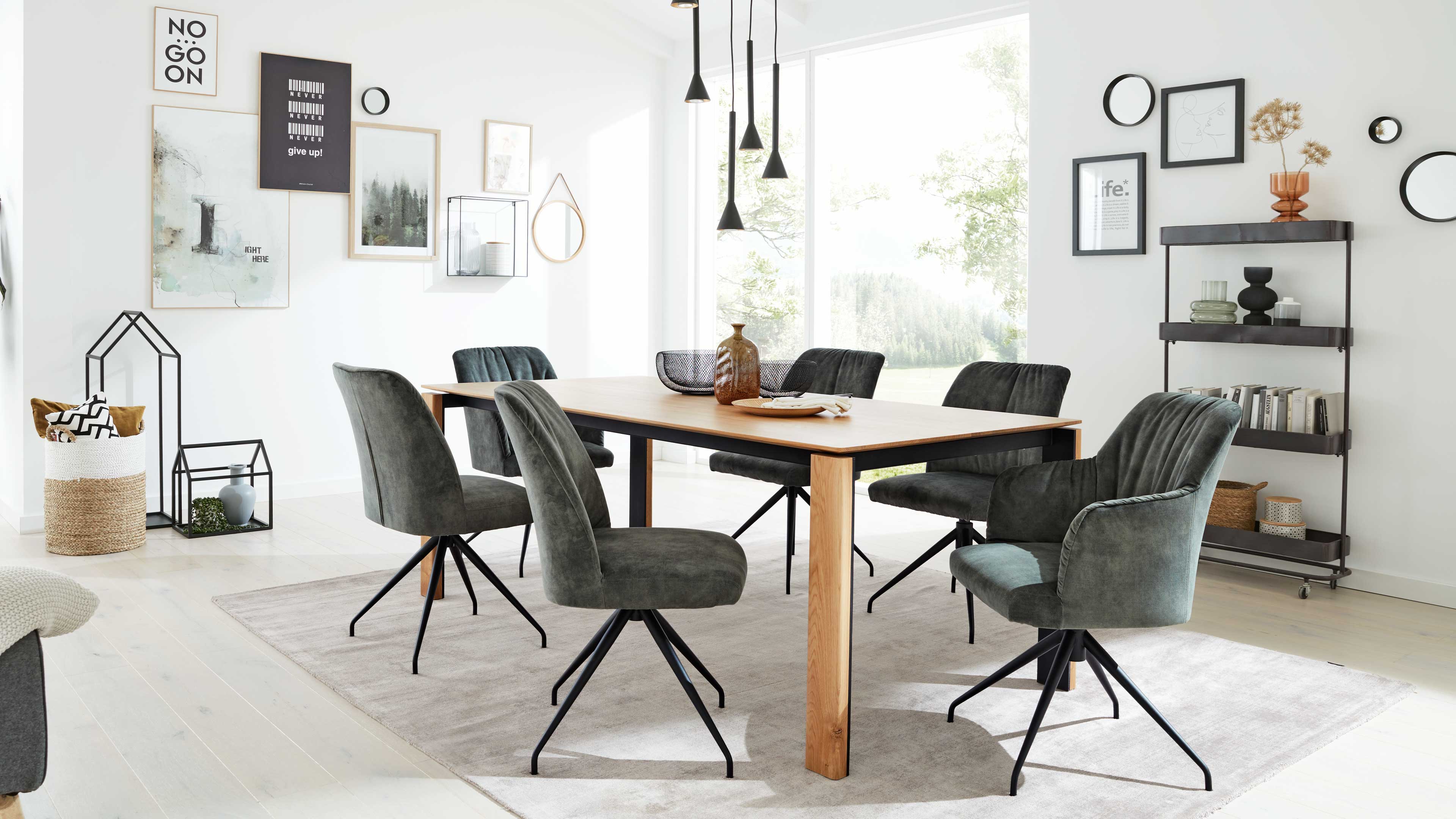 Holztisch mit sechs grauen, gepolsterten Drehstühlen auf hellem Teppich, darüber schwarze Pendelleuchten und Fensterwand.