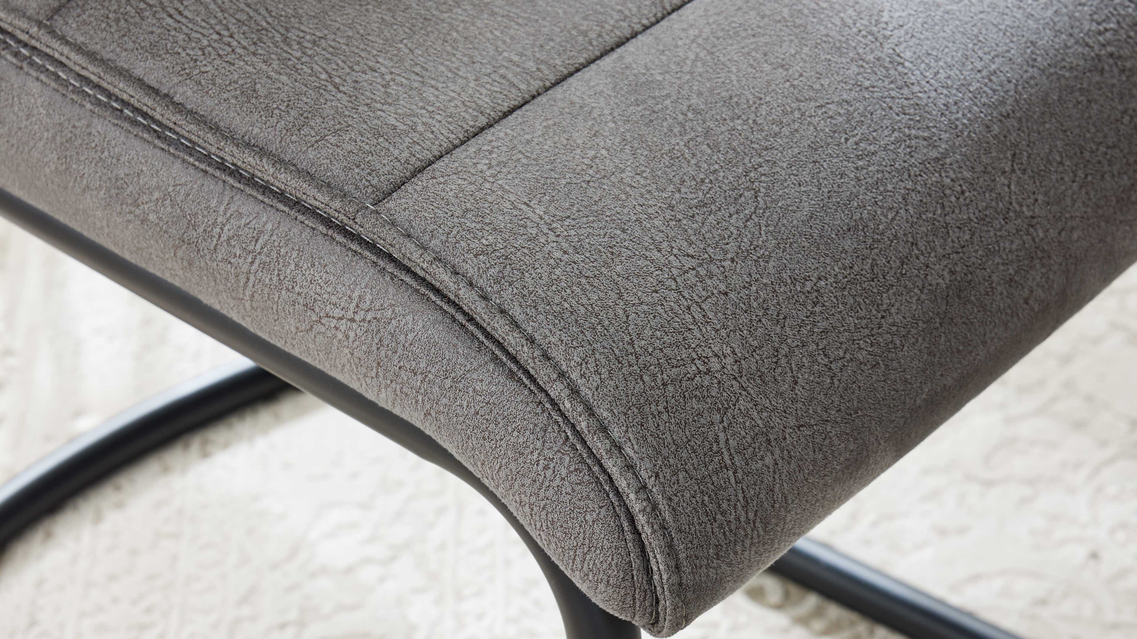 Nahaufnahme eines grauen, strukturierten Sitzpolsters mit abgesteppten Nähten und schwarzem gebogenem Metallgestell.