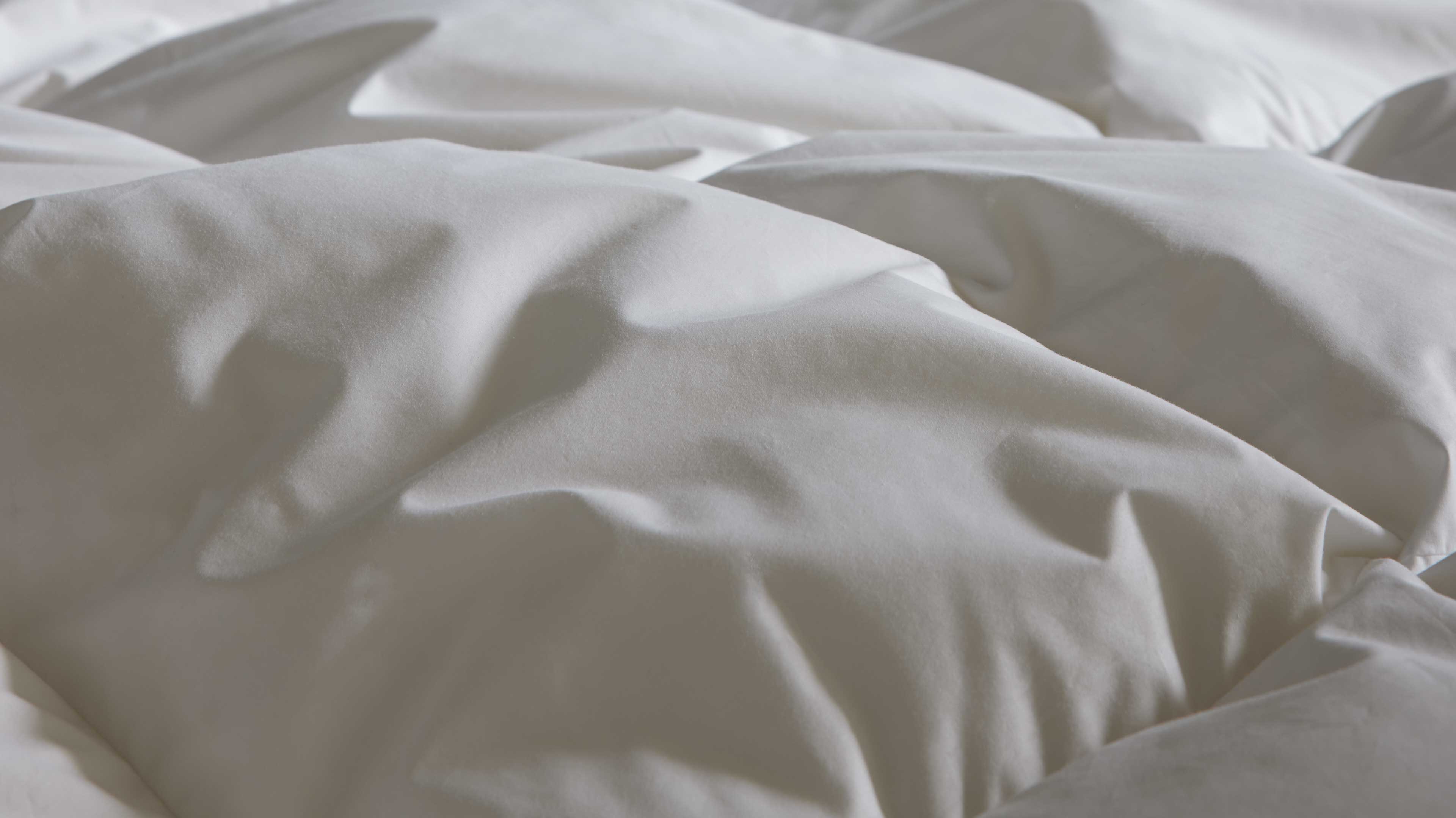 Nahaufnahme einer weißen gesteppelten Bettdecke mit wattierten Kammern, weichen Falten und feinen Schatten auf der Oberfläche.