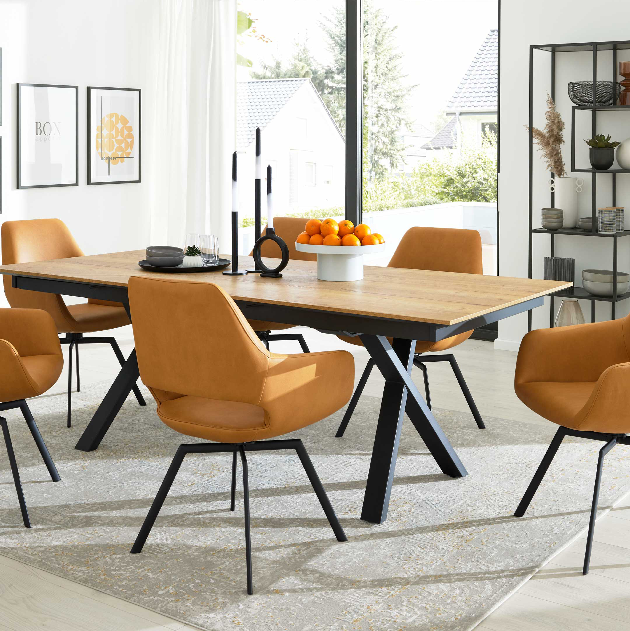 Rechteckiger Holztisch mit schwarzen Metallbeinen, umgeben von orangefarbenen Polsterstühlen, mit Obstschale, Kerzen und Regal.