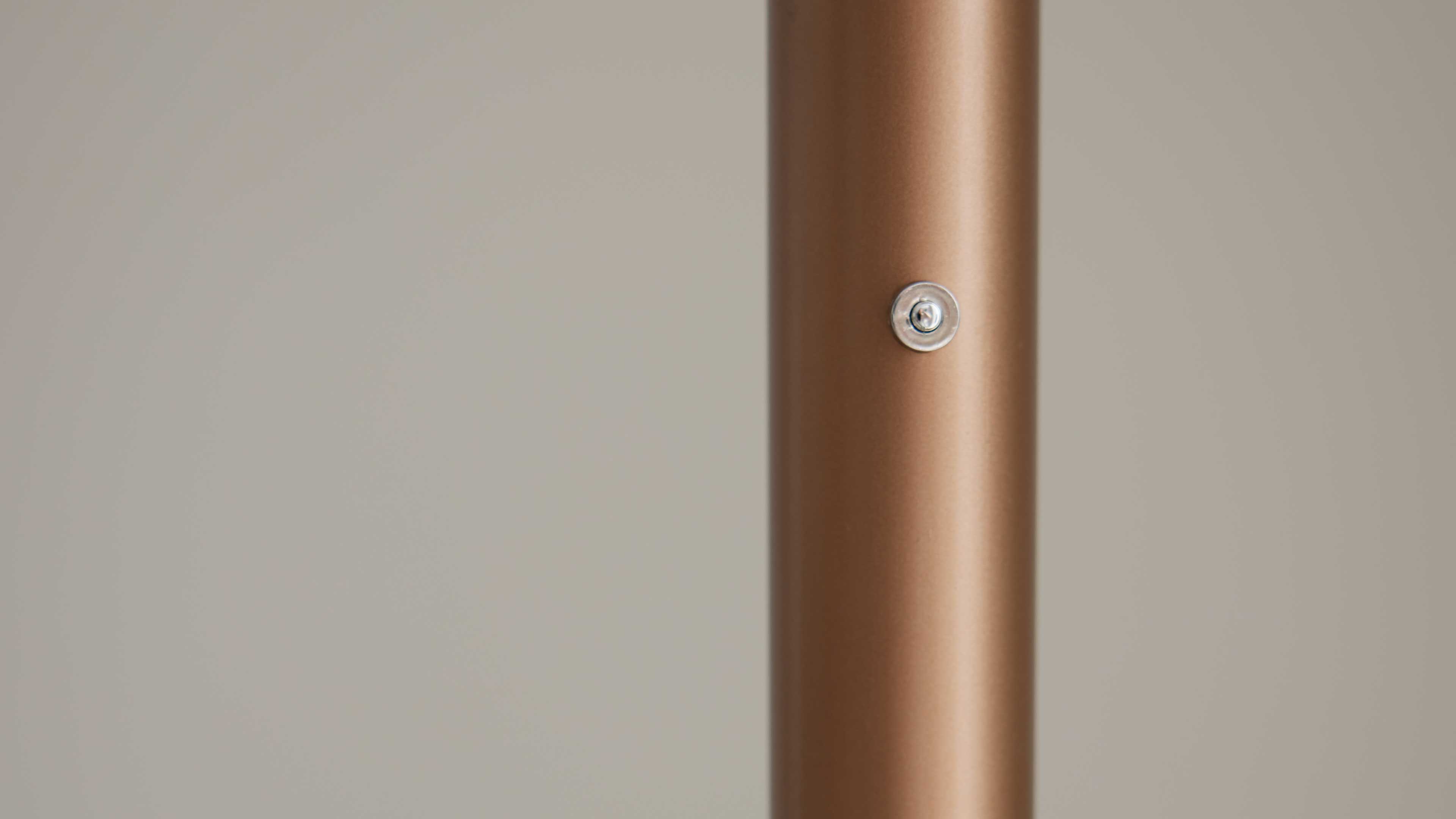 Zylindrische, bronzefarbene, matte Metallstange rechtsseitig mit einem kleinen runden Metallknopf und einfarbigem hellgrauem Hintergrund.