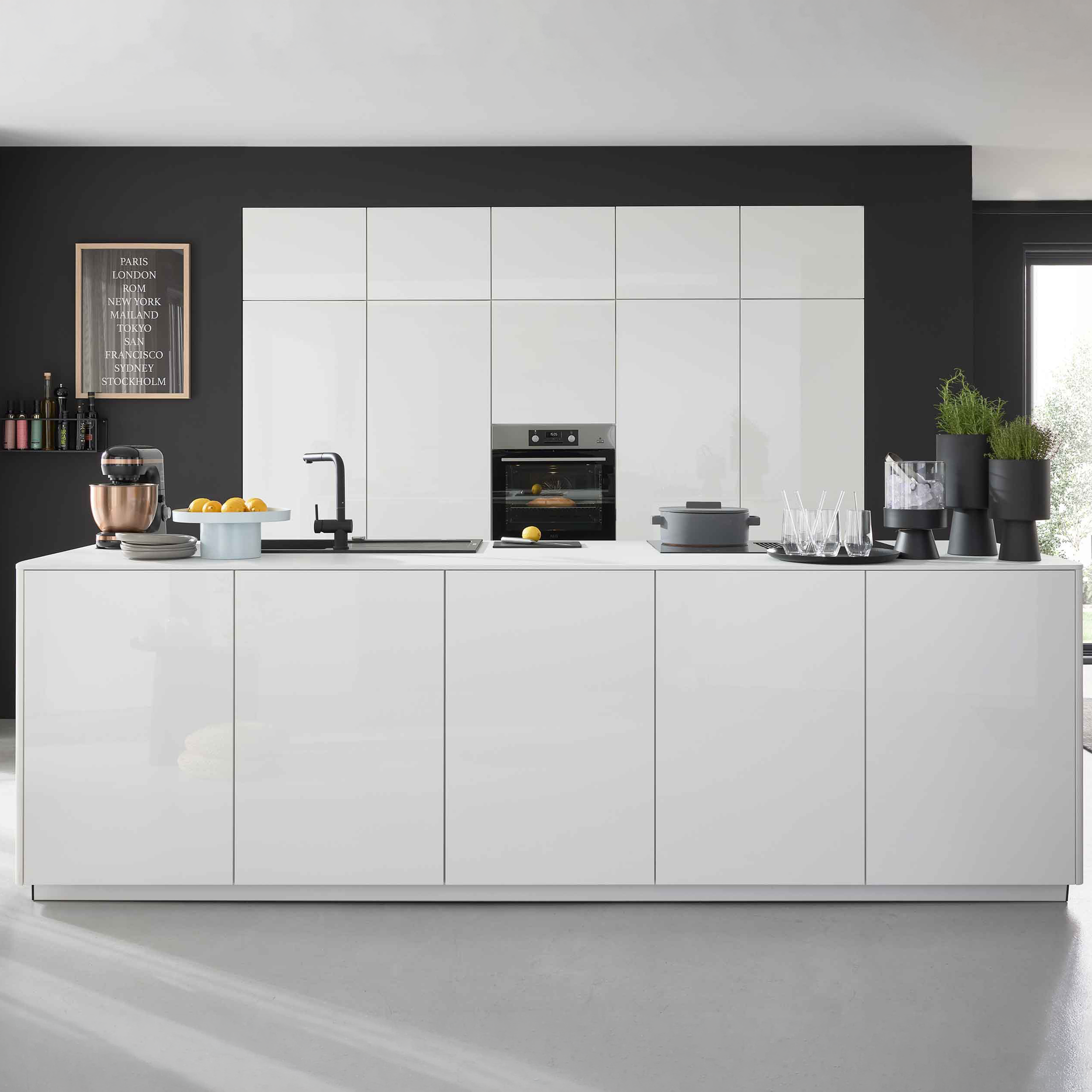 Weiße Kücheninsel mit Spüle und schwarzer Armatur, Mixer, Schale mit Zitronen und Gläsern, im Hintergrund weiße Hochschränke mit Ofen.