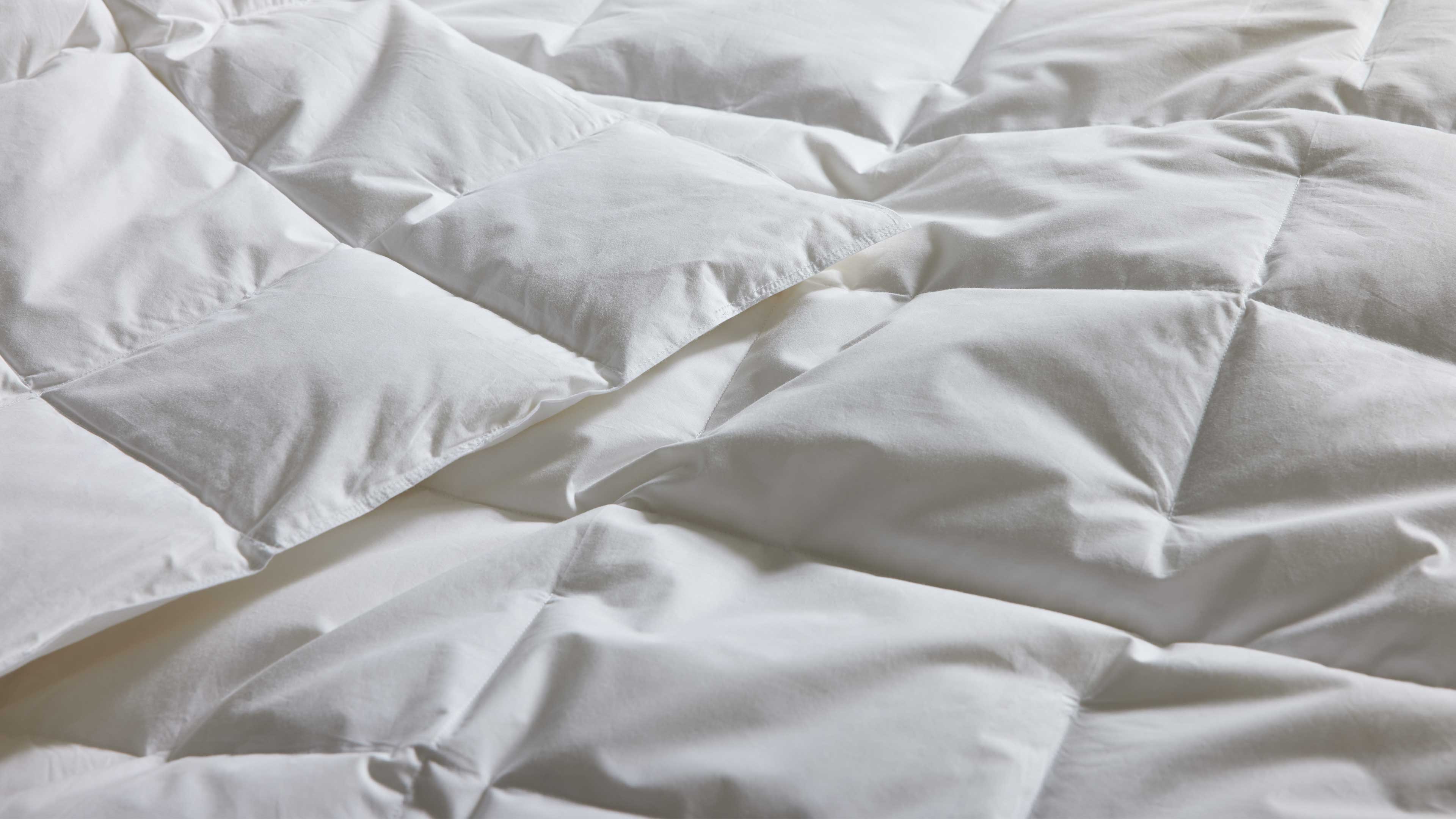 Gesteppte weiße Bettdecke mit quadratischen Kammern, leicht aufgebauscht, mit sanften Falten und Schatten.