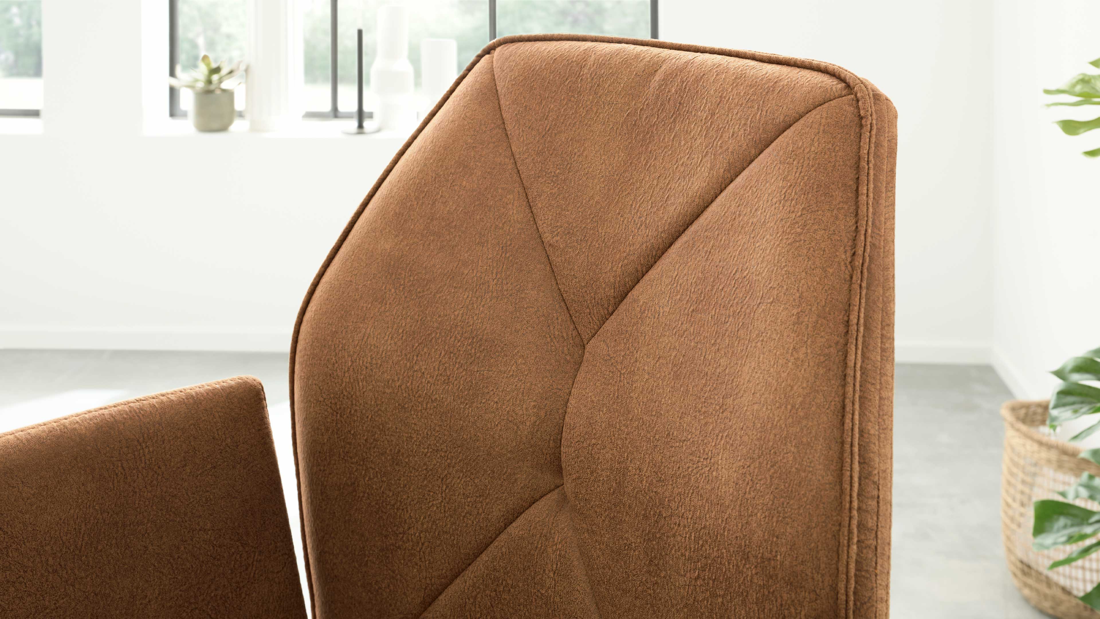 Braune, gepolsterte Rückenlehne und Armlehne mit geometrischen Nähten, im Hintergrund Fenster und Pflanze.