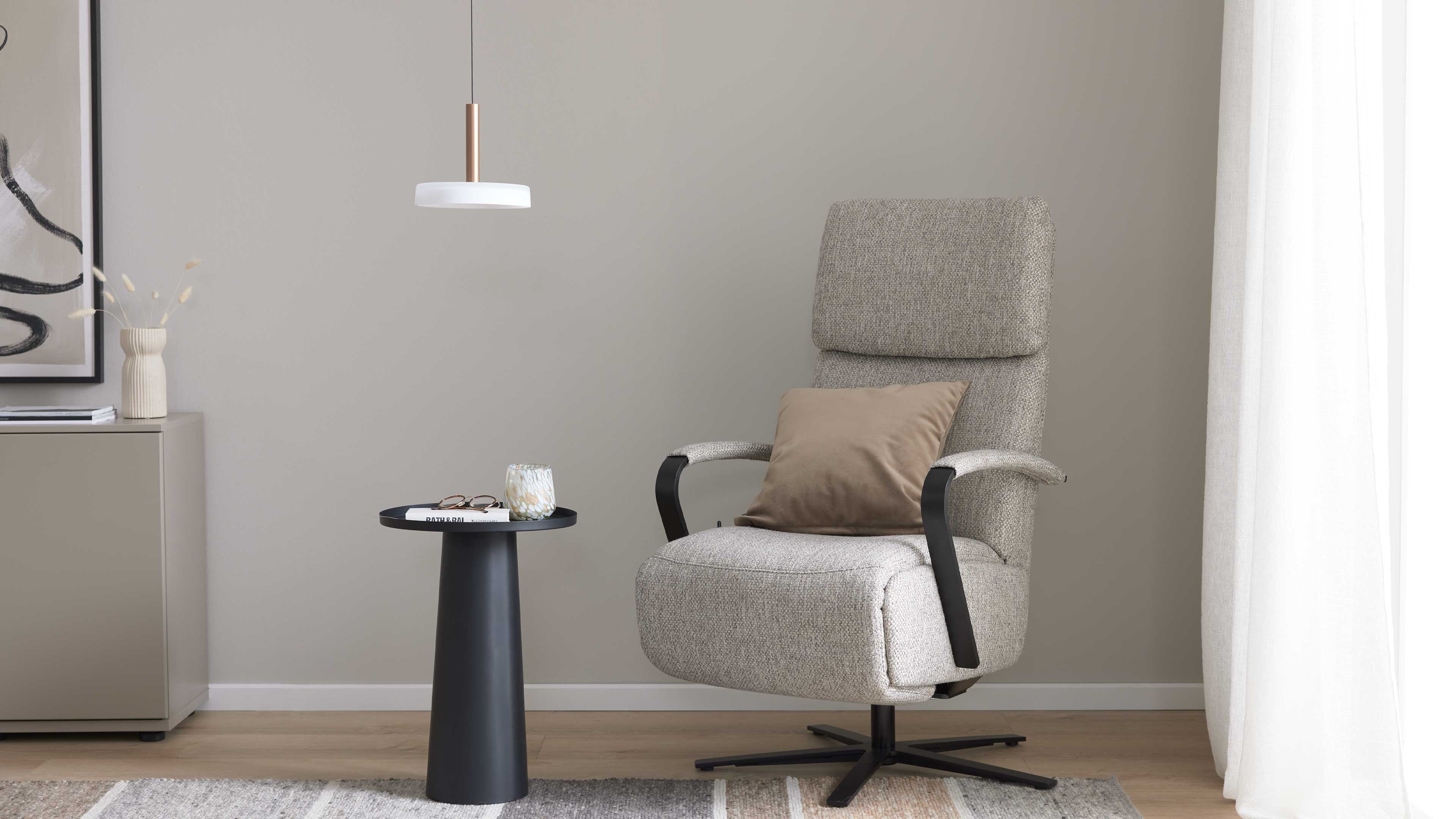 Hellbeiger, gepolsterter Drehsessel mit schwarzem Gestell und braunem Kissen, daneben schwarzer runder Beistelltisch.