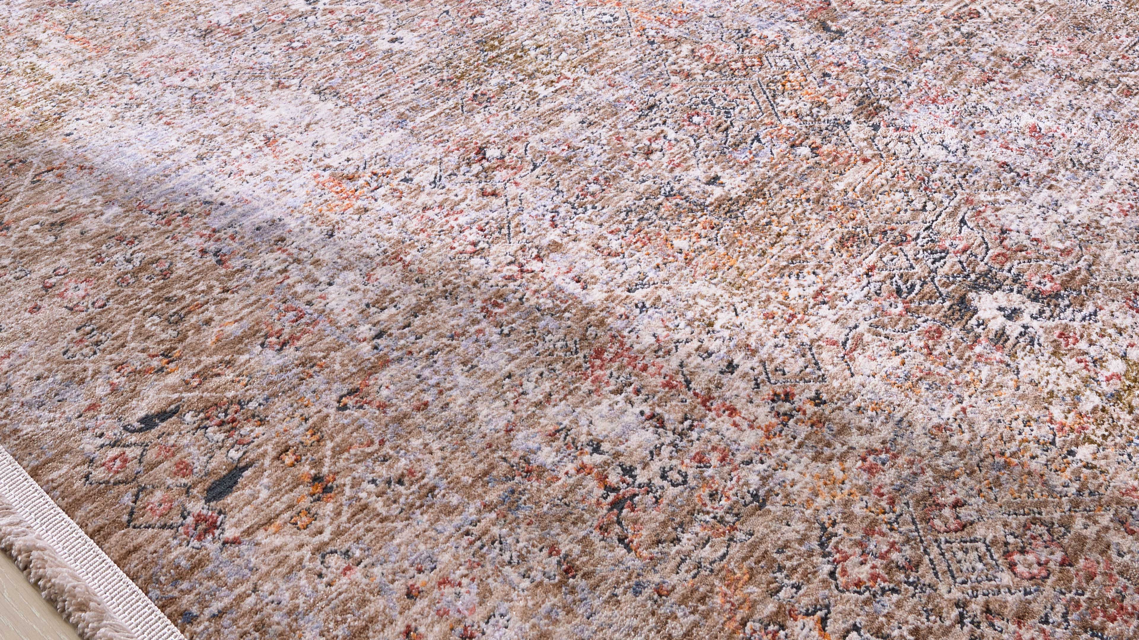 Beiger Teppich mit verblasstem floralen und geometrischen Muster in Rost-, Grau- und Weißtönen, Fransen links und diagonischer Lichtfleck.